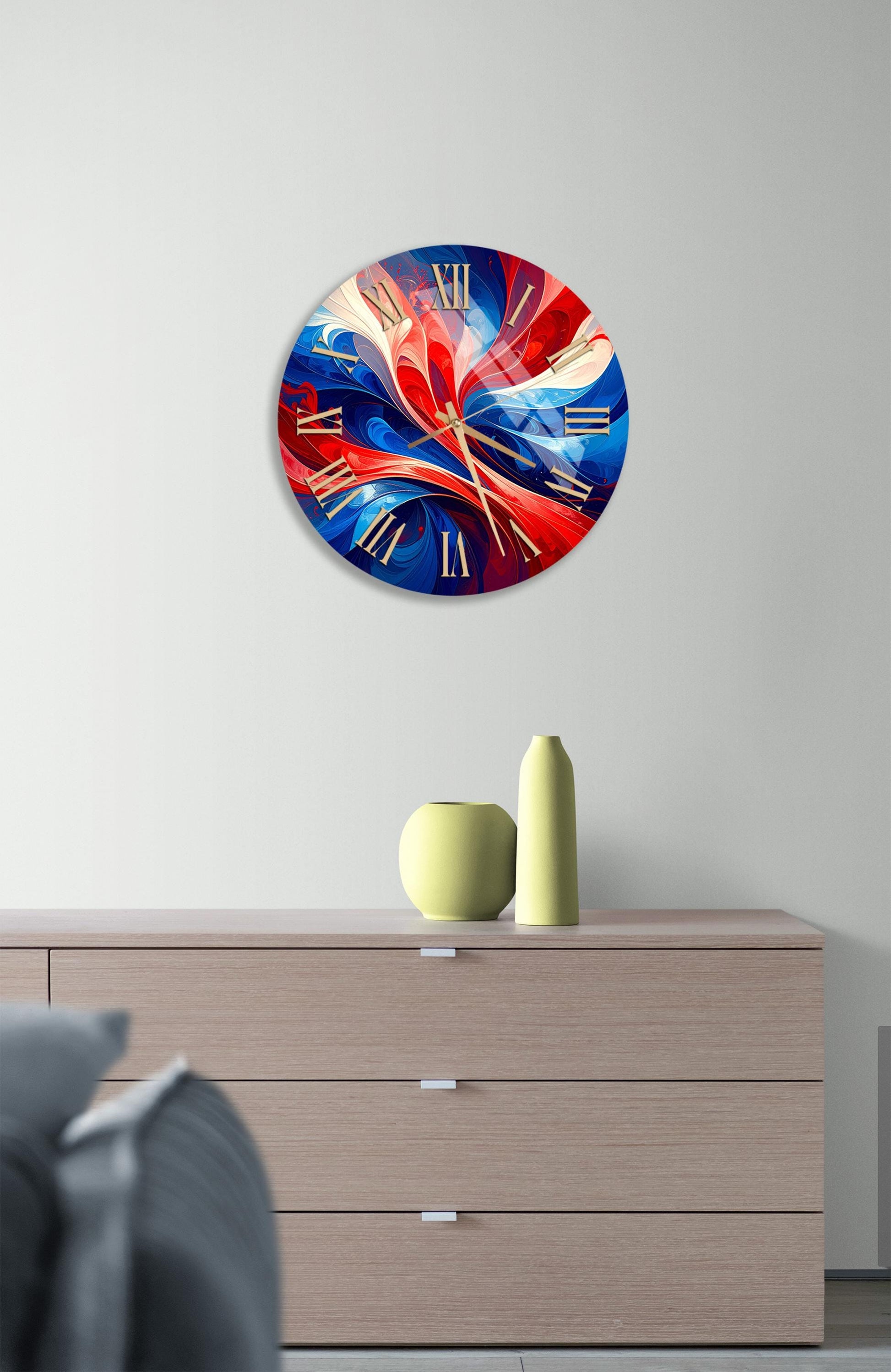 a modern clock with a vibrant, abstract design in red, blue, and yellow colors, hanging on a wall above a wooden dresser.