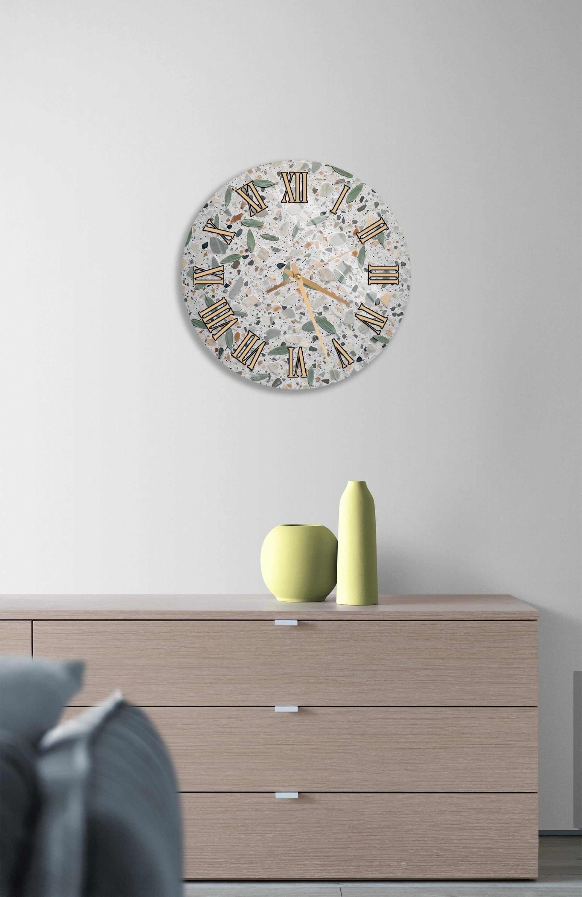 a modern living room with a large round wall clock displaying Roman numerals, a wooden dresser with a vase and a small green pot, and a gray couch in the background.