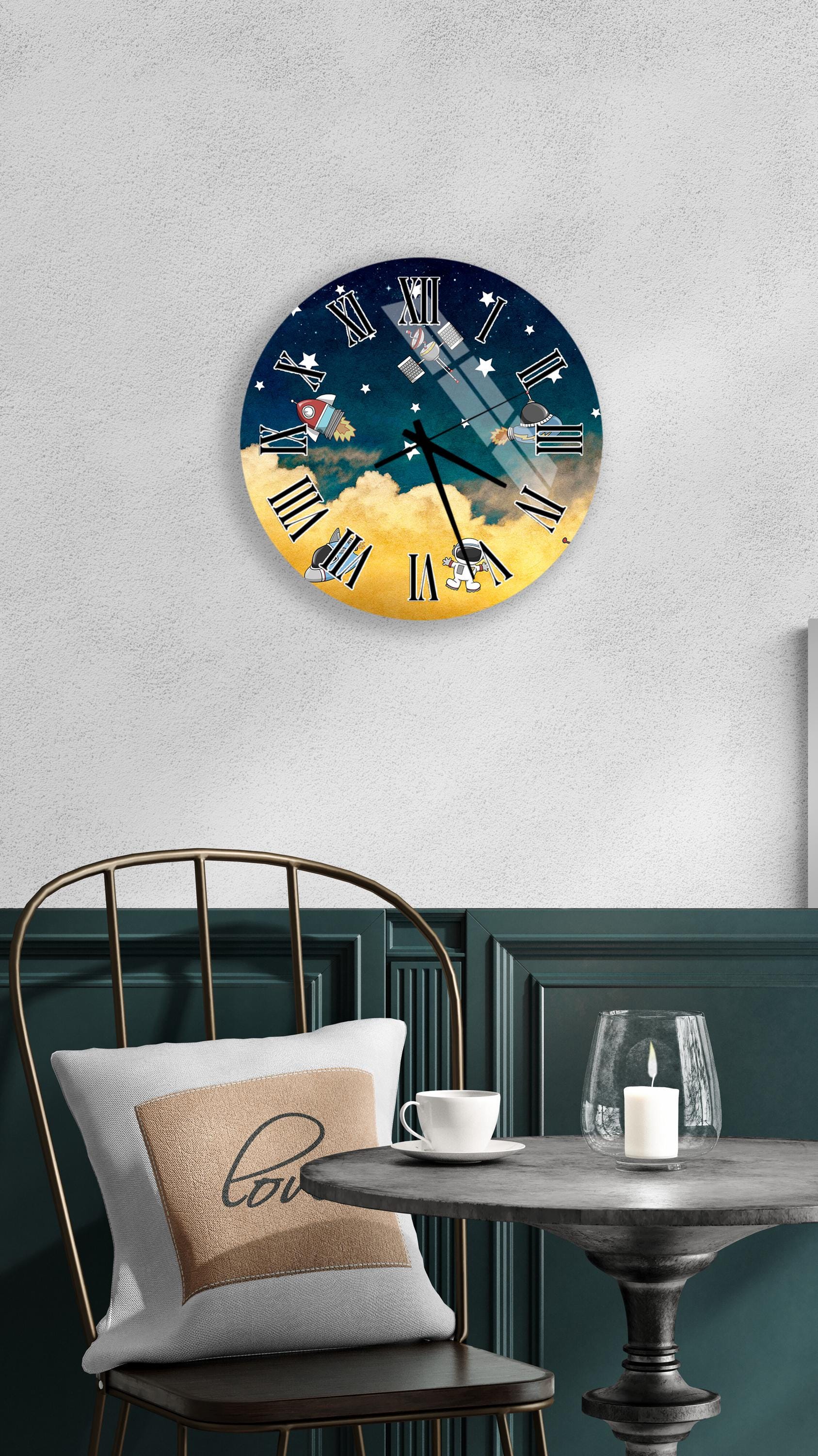 a wall clock with a night sky design, a white table with a candle and a cup, and a chair with a pillow.