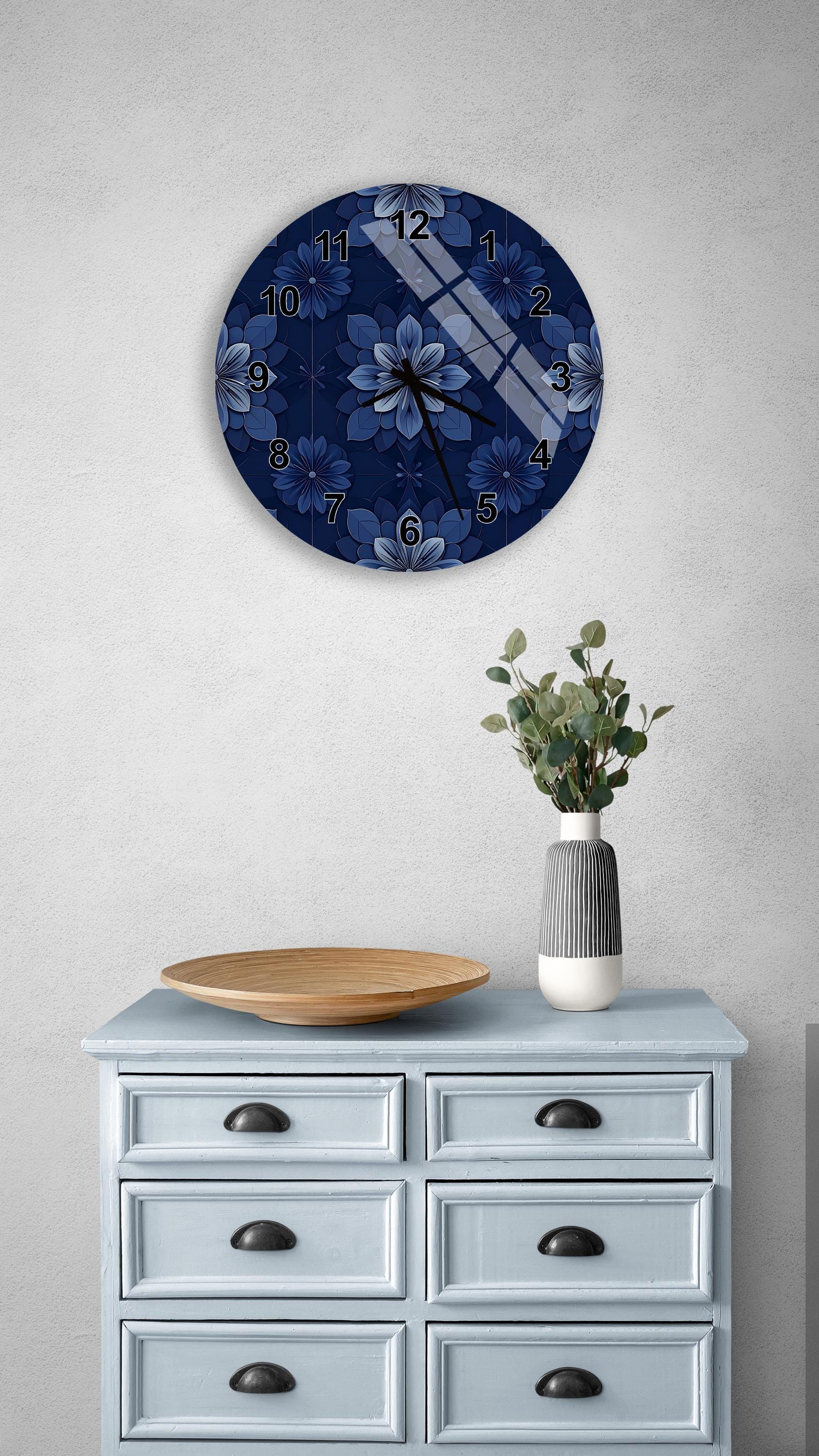 a blue wall clock with a floral design, a wooden bowl, and a vase with greenery on a light blue dresser.