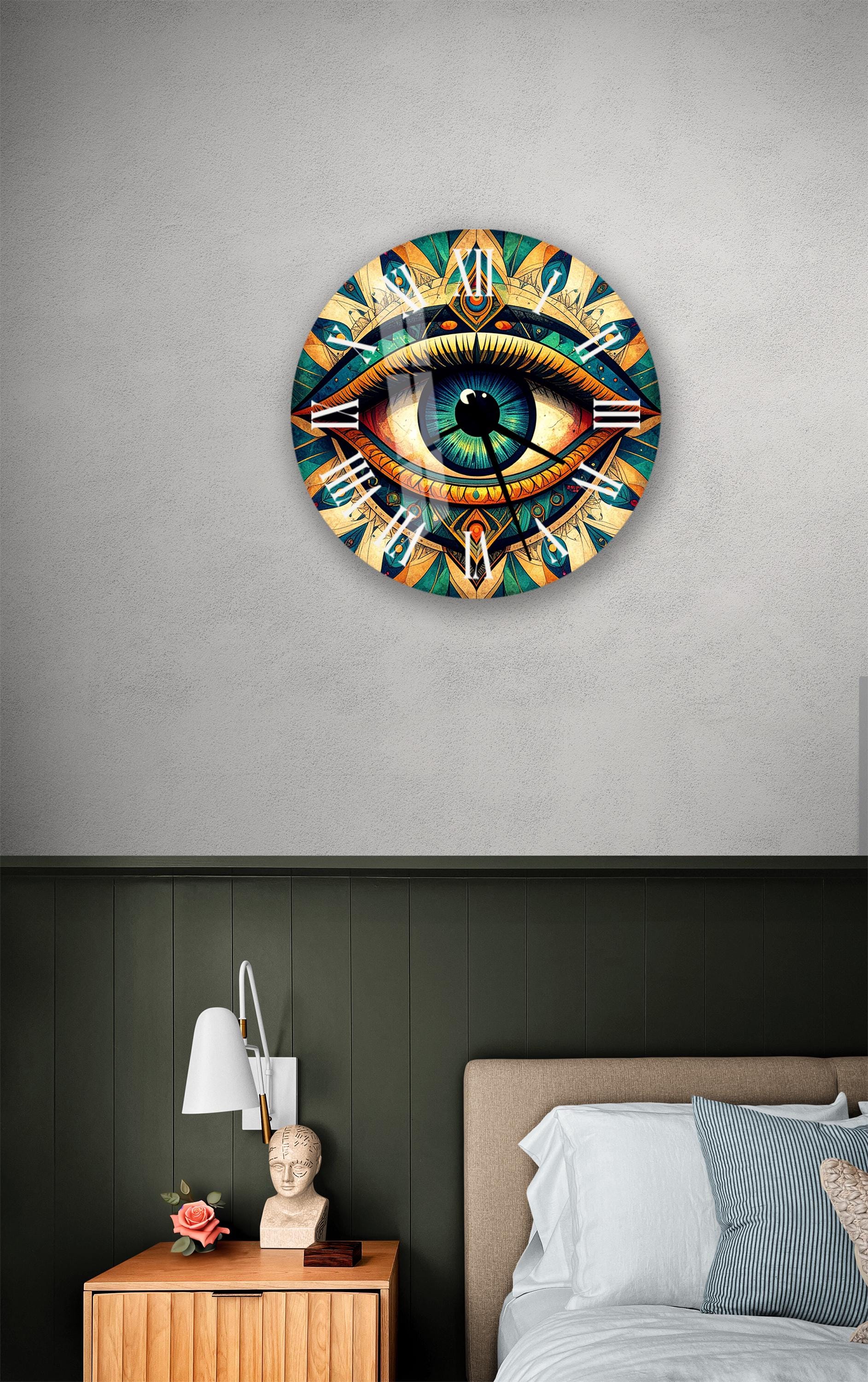 a wall clock with a large eye design on it, mounted on a wall above a bedside table with a lamp and a statue.