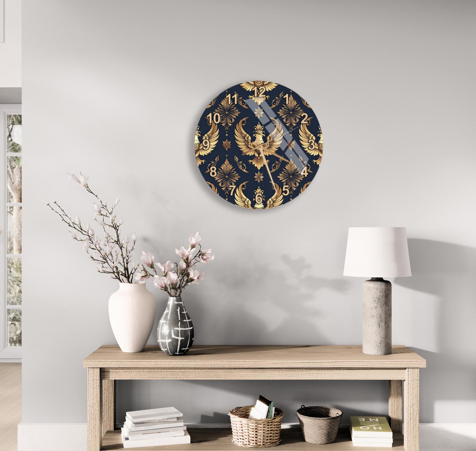 a wall clock with a gold and navy blue design, a wooden table with a lamp, a vase with flowers, and some books on a shelf.