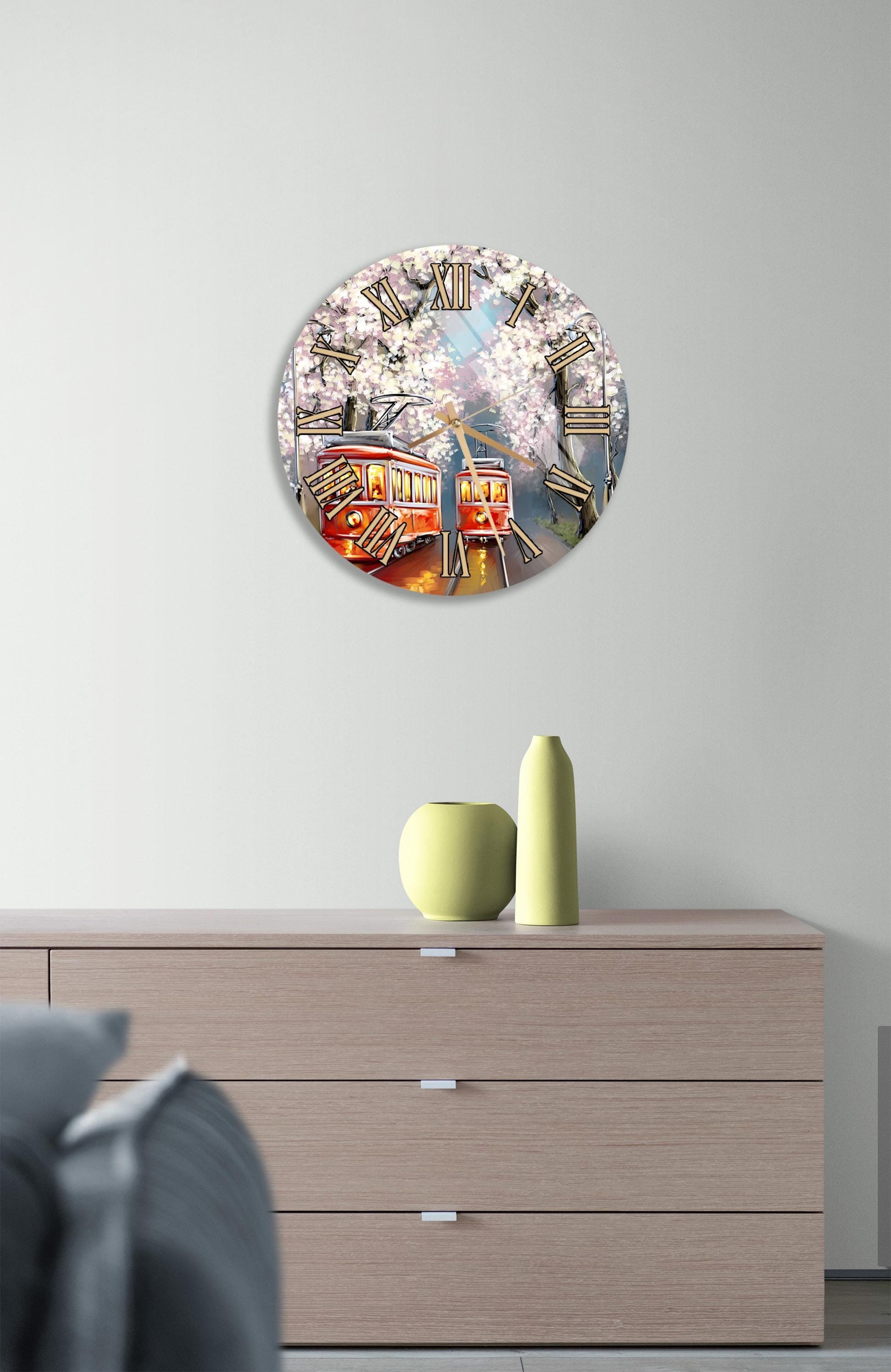 a round clock with a floral design hanging on a wall above a wooden dresser with three drawers.