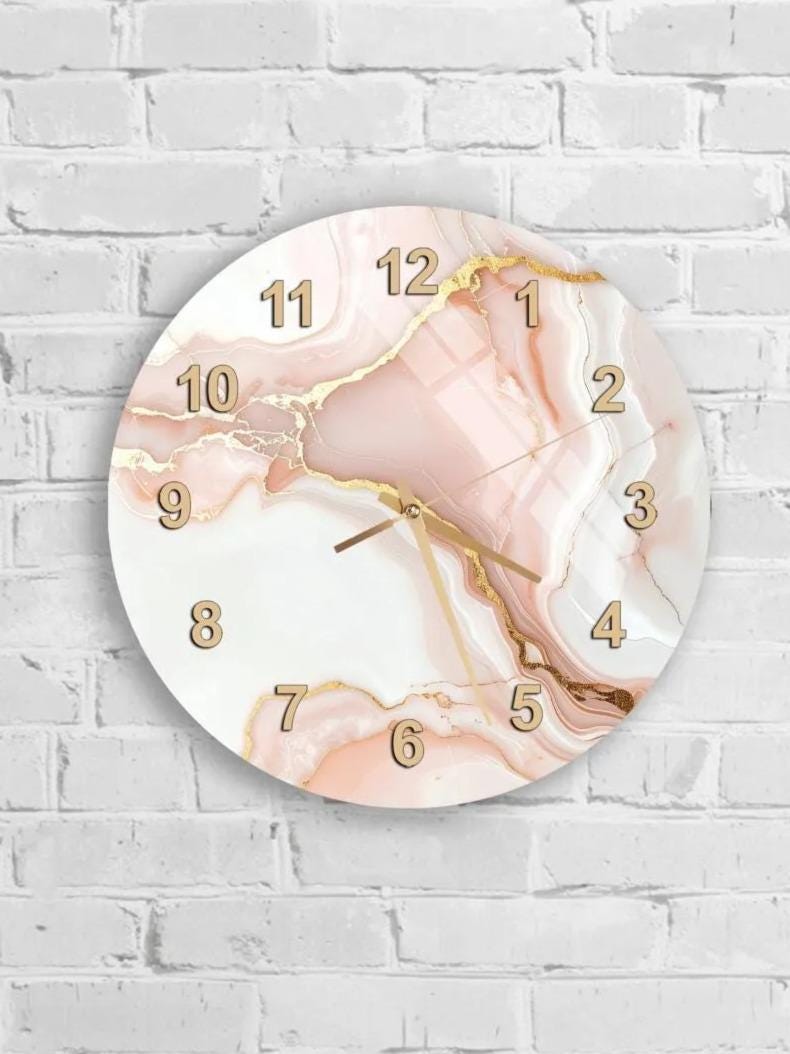 A round wall clock with a marble-like design and gold numbers is mounted on a white brick wall.