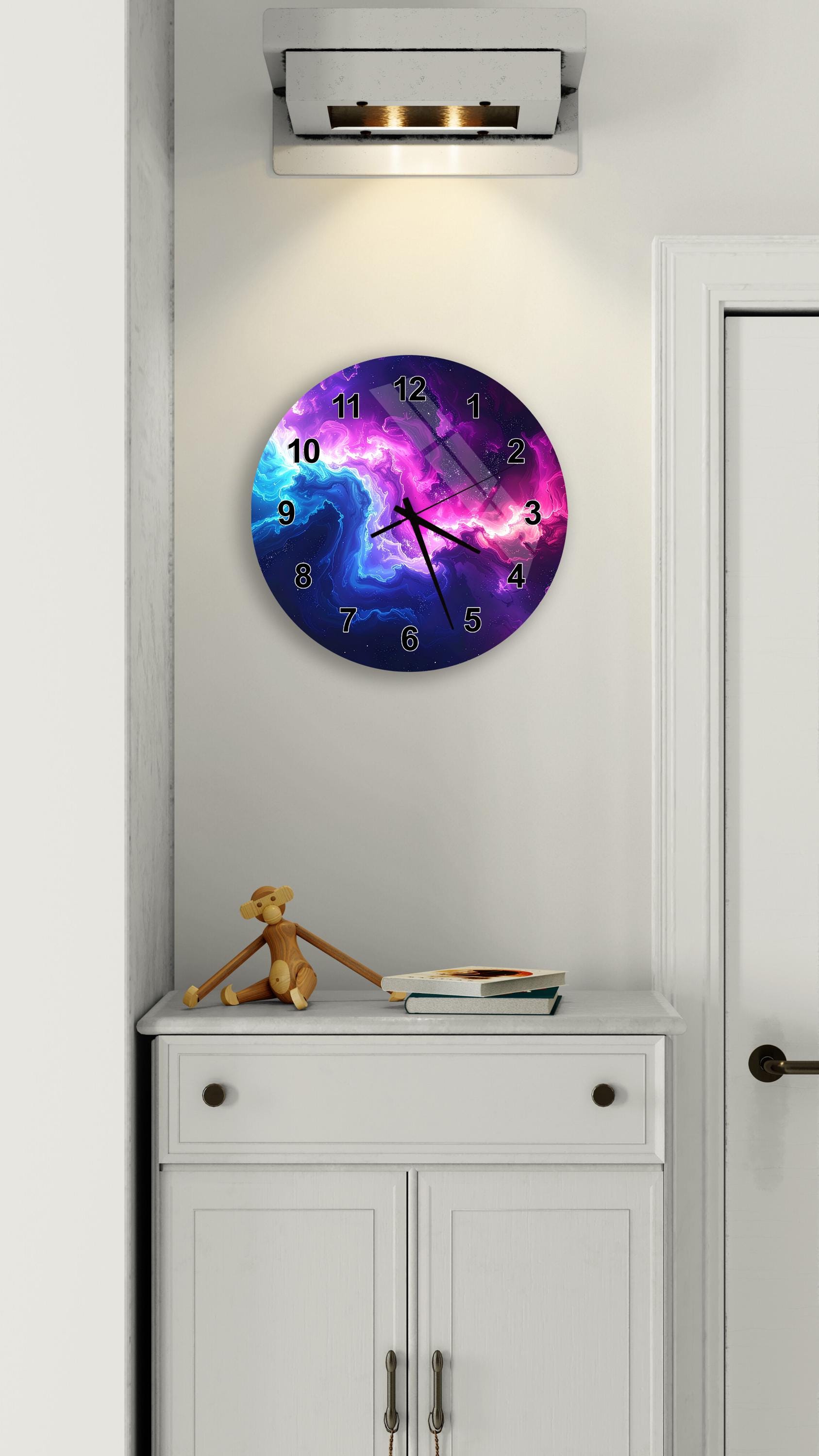 a wall clock with a colorful galaxy design, mounted on a white wall above a white cabinet.