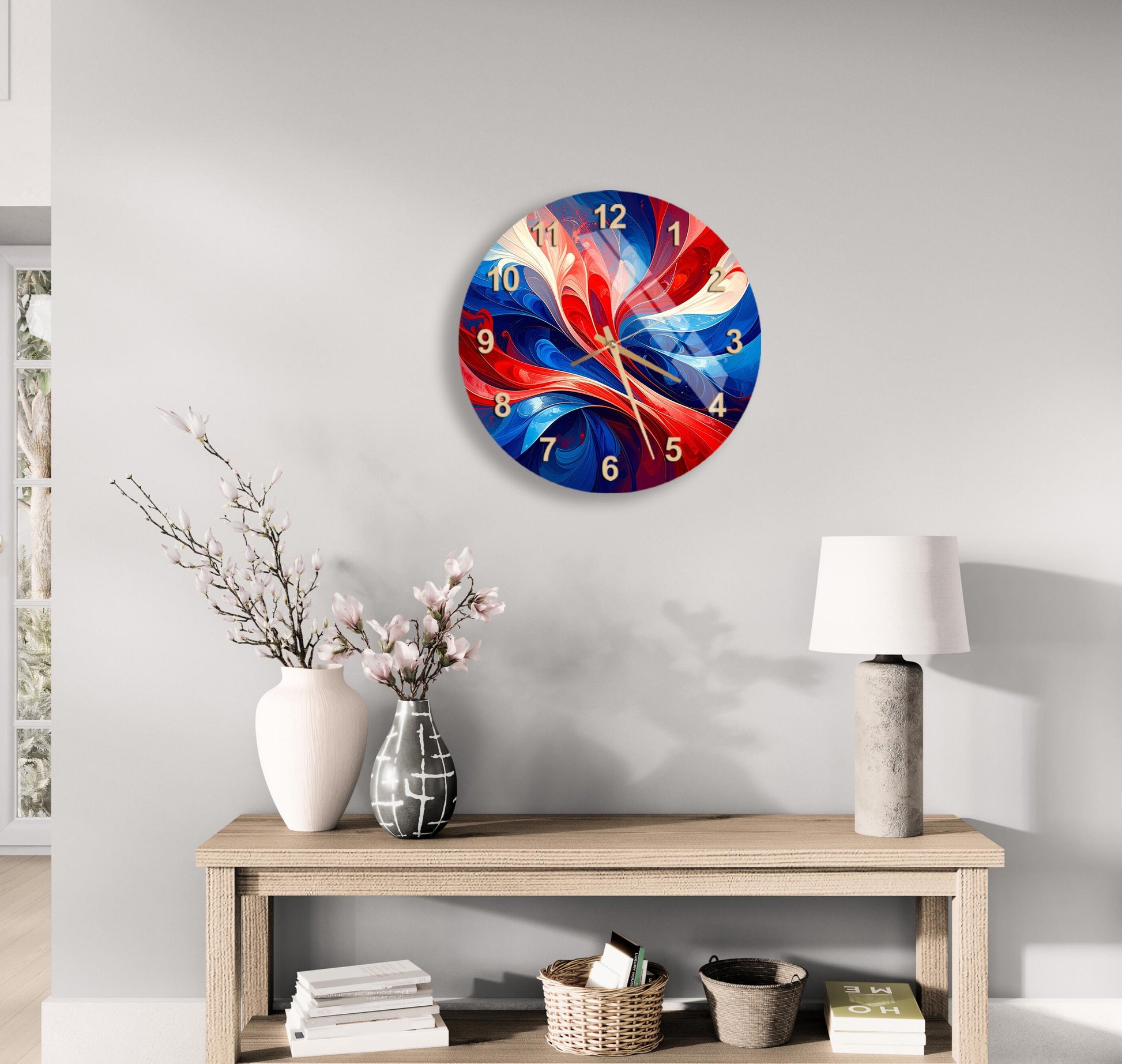 a modern wall clock with a vibrant, abstract design in red, blue, and white colors, hanging above a wooden table with a lamp and decorative items.