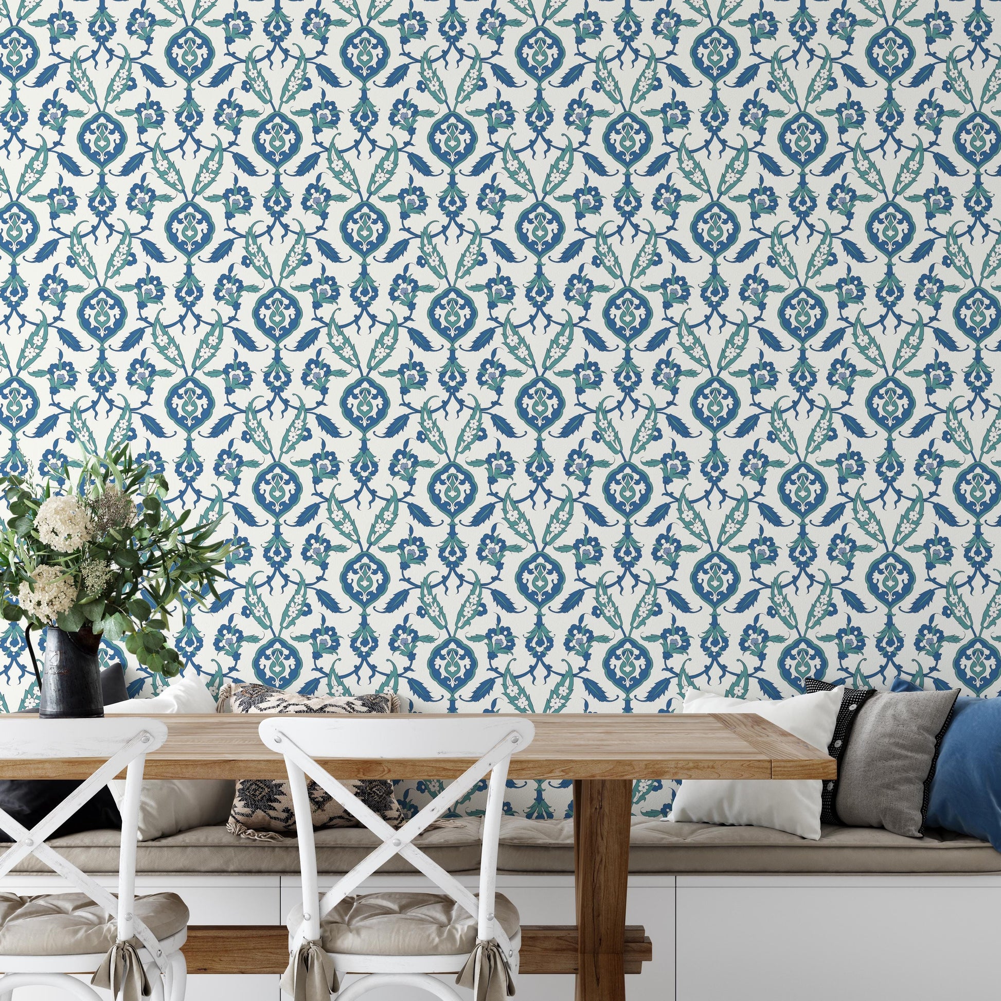 a dining area with a wooden table and white chairs, set against a wall with a blue and white floral pattern wallpaper. A vase of flowers is placed on the table, adding a touch of natural beauty to the scene.