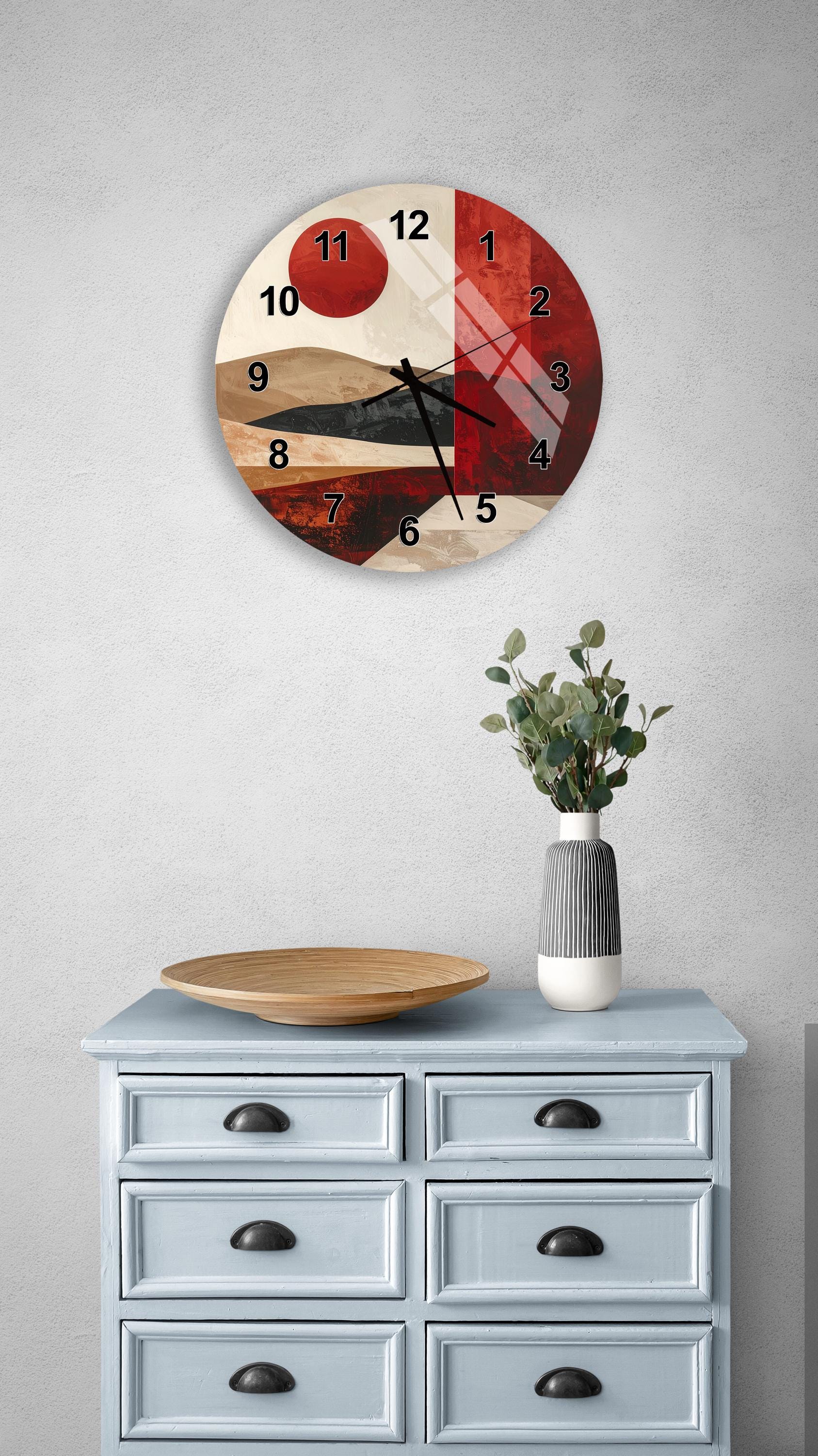 a wall clock with a red and brown abstract design, mounted on a wall above a light blue dresser with six drawers. The dresser also has a vase with greenery and a wooden bowl on top.