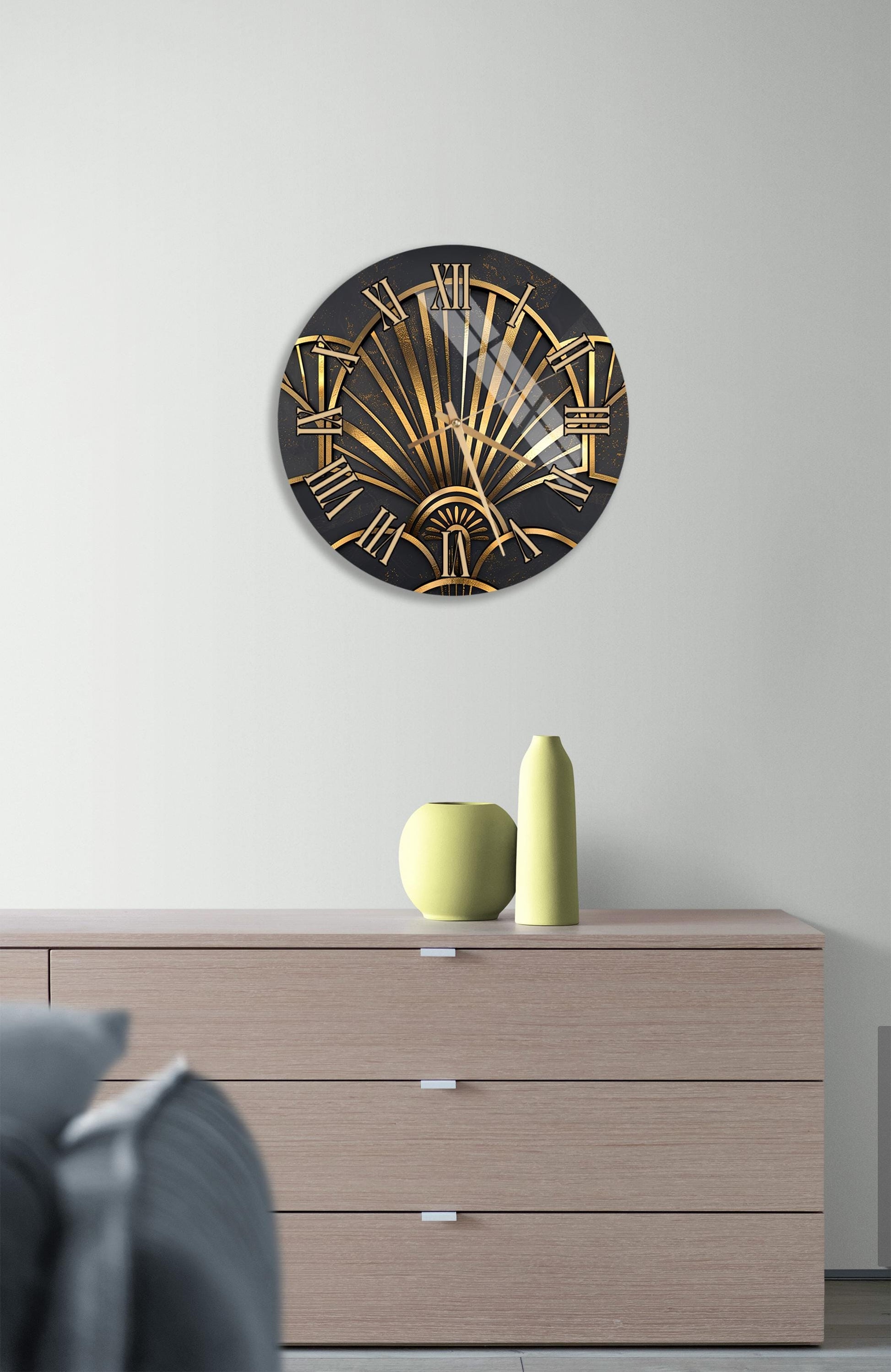 a modern art deco style clock with a black and gold design, mounted on a white wall above a wooden dresser with three drawers.