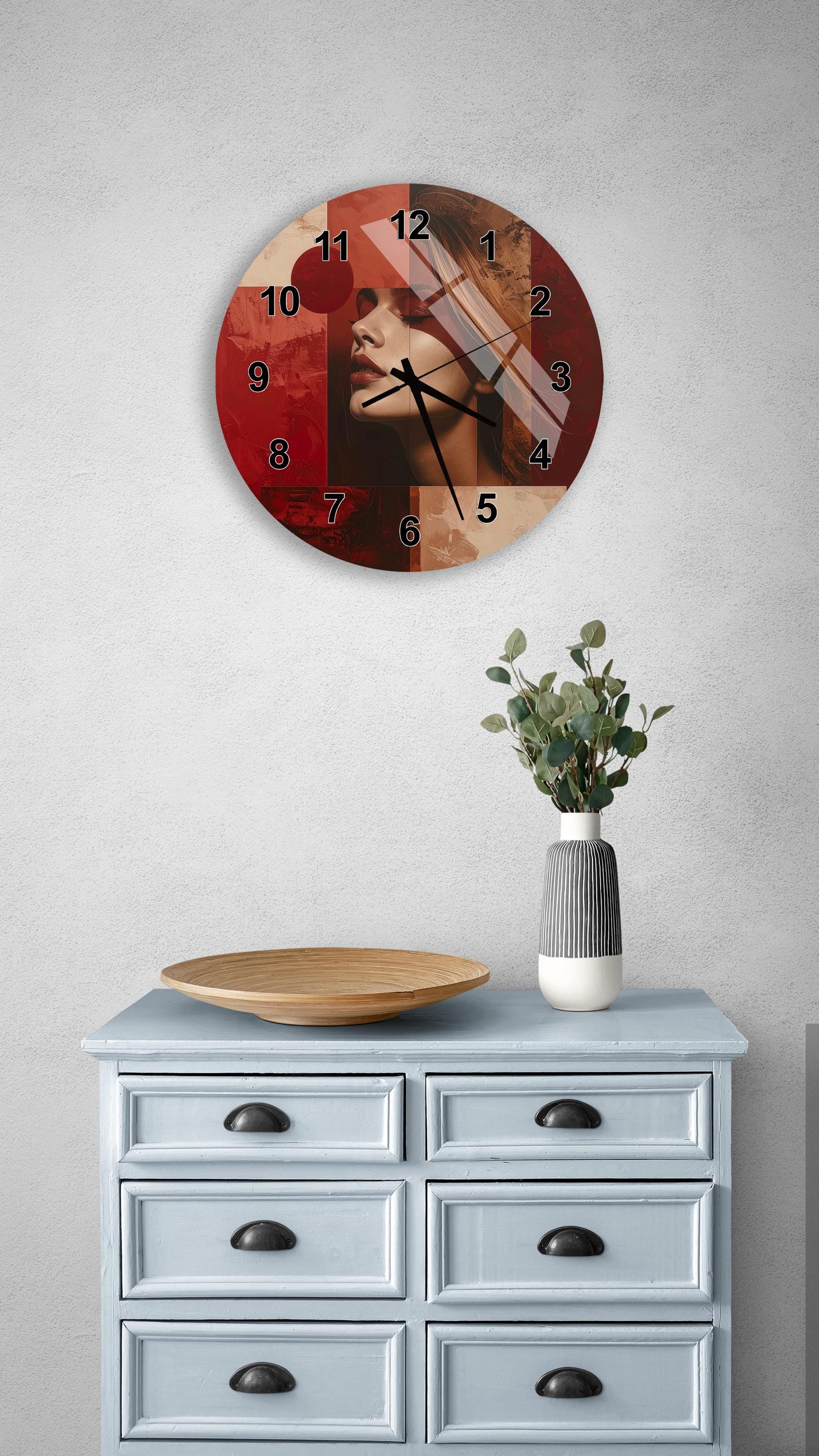 a wall clock with a red and black design, mounted on a wall above a light blue dresser with six drawers. The dresser also has a vase with greenery on it, and there is a wooden bowl on the dresser.