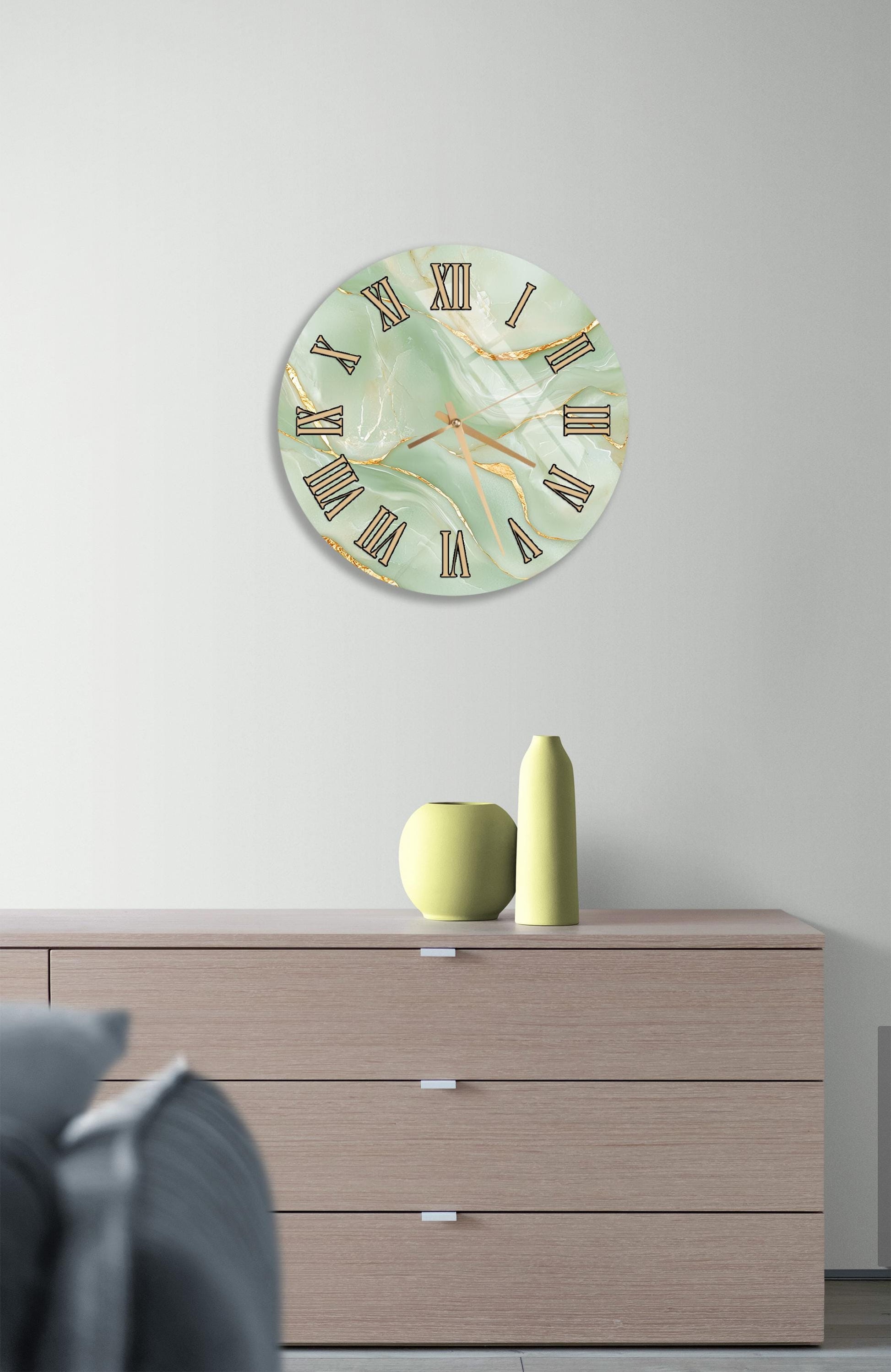 a wall clock with a marble-like green and gold design, mounted on a wall above a wooden dresser with three drawers.