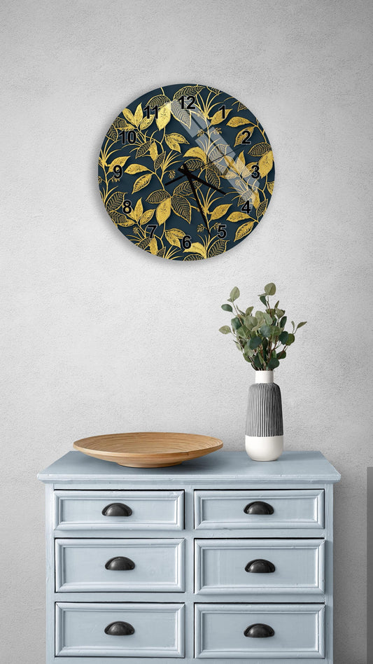 a wall clock with a gold leaf design, a wooden bowl, and a vase with greenery on a light blue dresser.