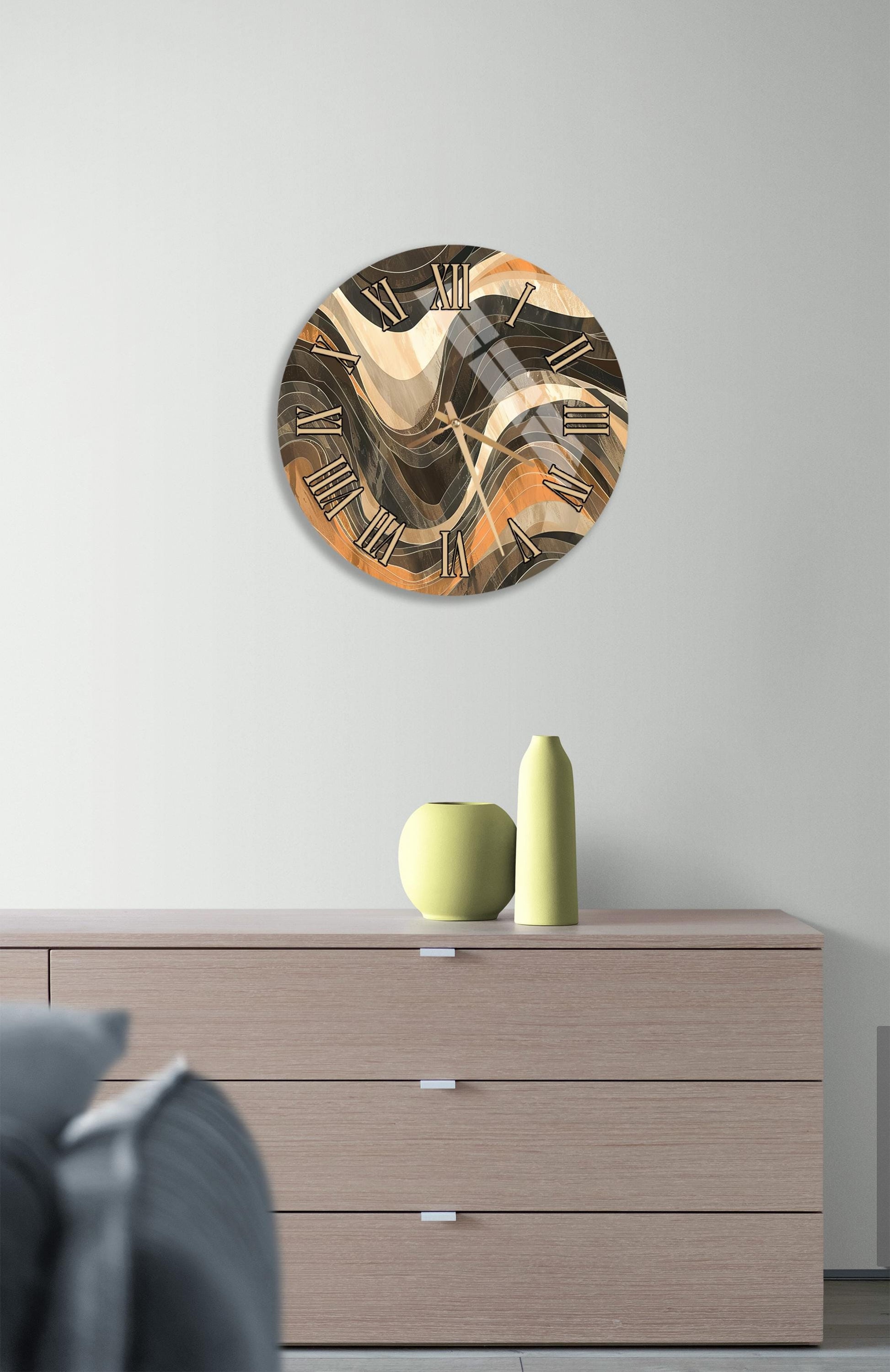 a modern clock with a unique abstract design, mounted on a wall above a wooden dresser. The dresser has three drawers and contains a yellow vase and a green vase, adding a touch of color to the minimalist setting.