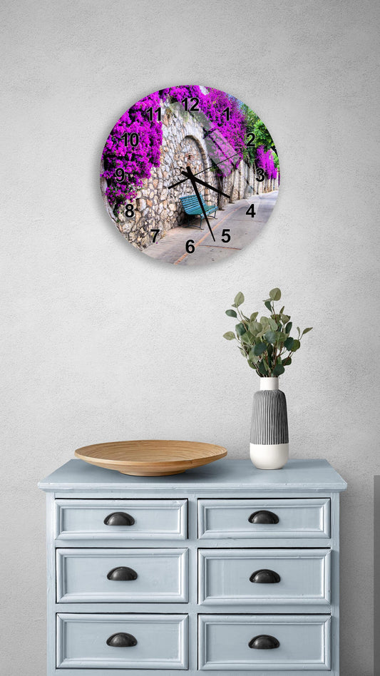 a wall clock with a vibrant purple floral design, mounted on a wall above a light blue dresser with six drawers. The dresser also has a small vase with greenery and a wooden bowl on top.