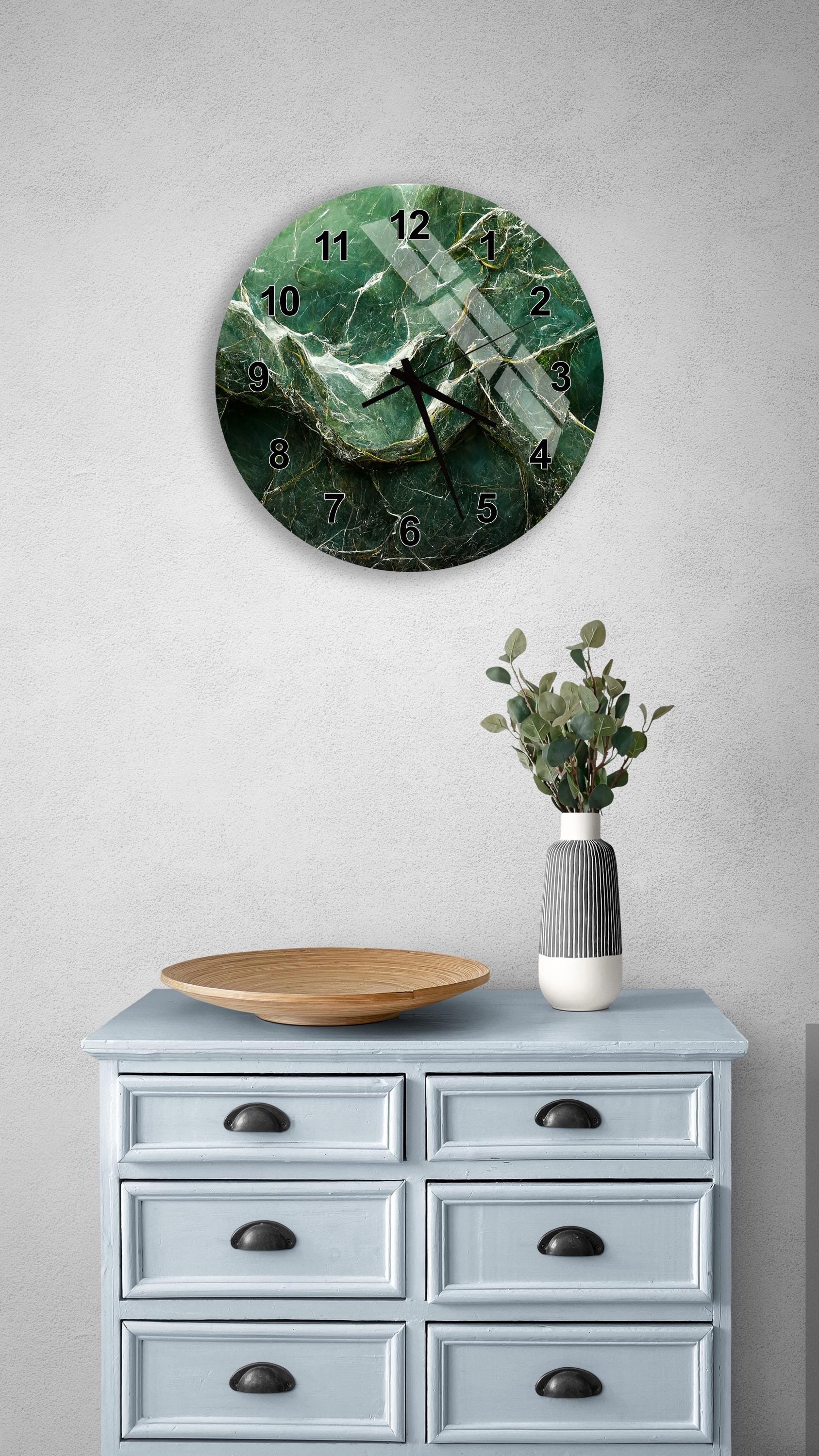 a wall clock with a green marble design, a wooden bowl, and a vase with greenery on a light blue dresser.