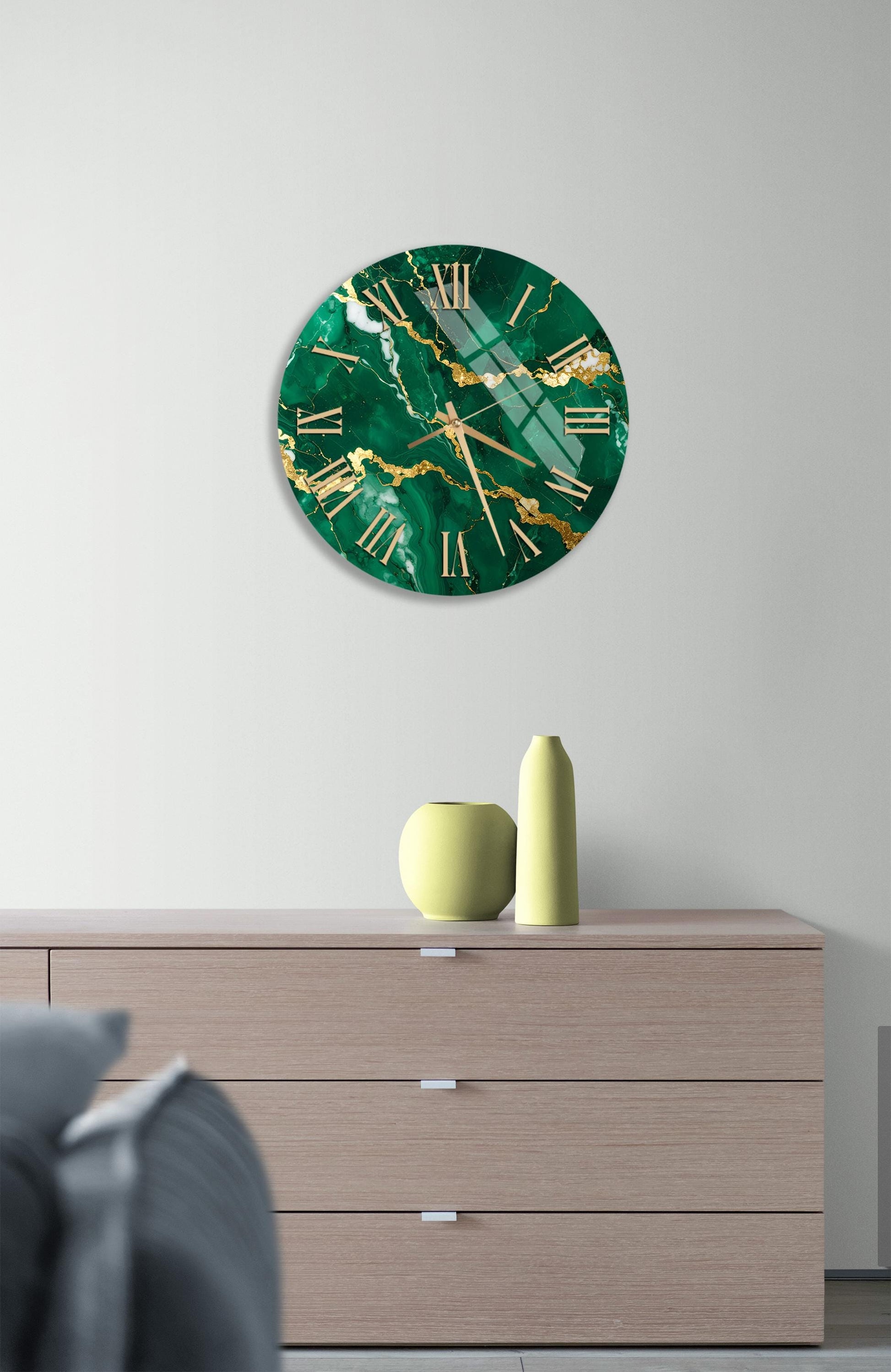 a modern living room with a large green marble clock hanging on the wall above a wooden dresser. The dresser has three drawers and a vase on top.