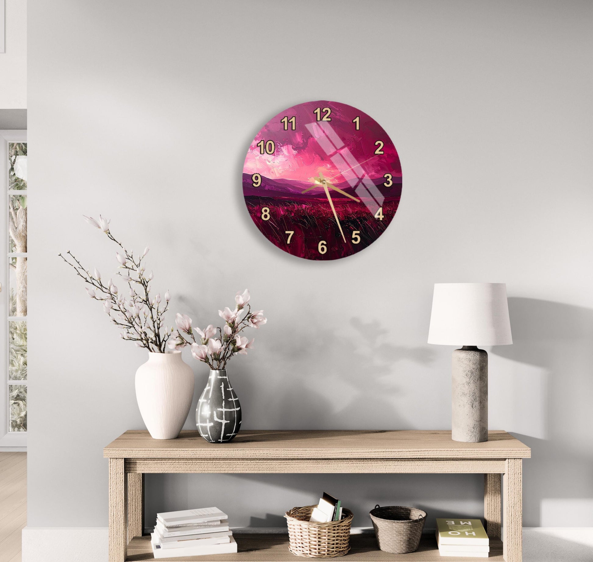 a wall clock with a pink and purple design, a wooden table with a lamp, a vase with flowers, and some books on a shelf.