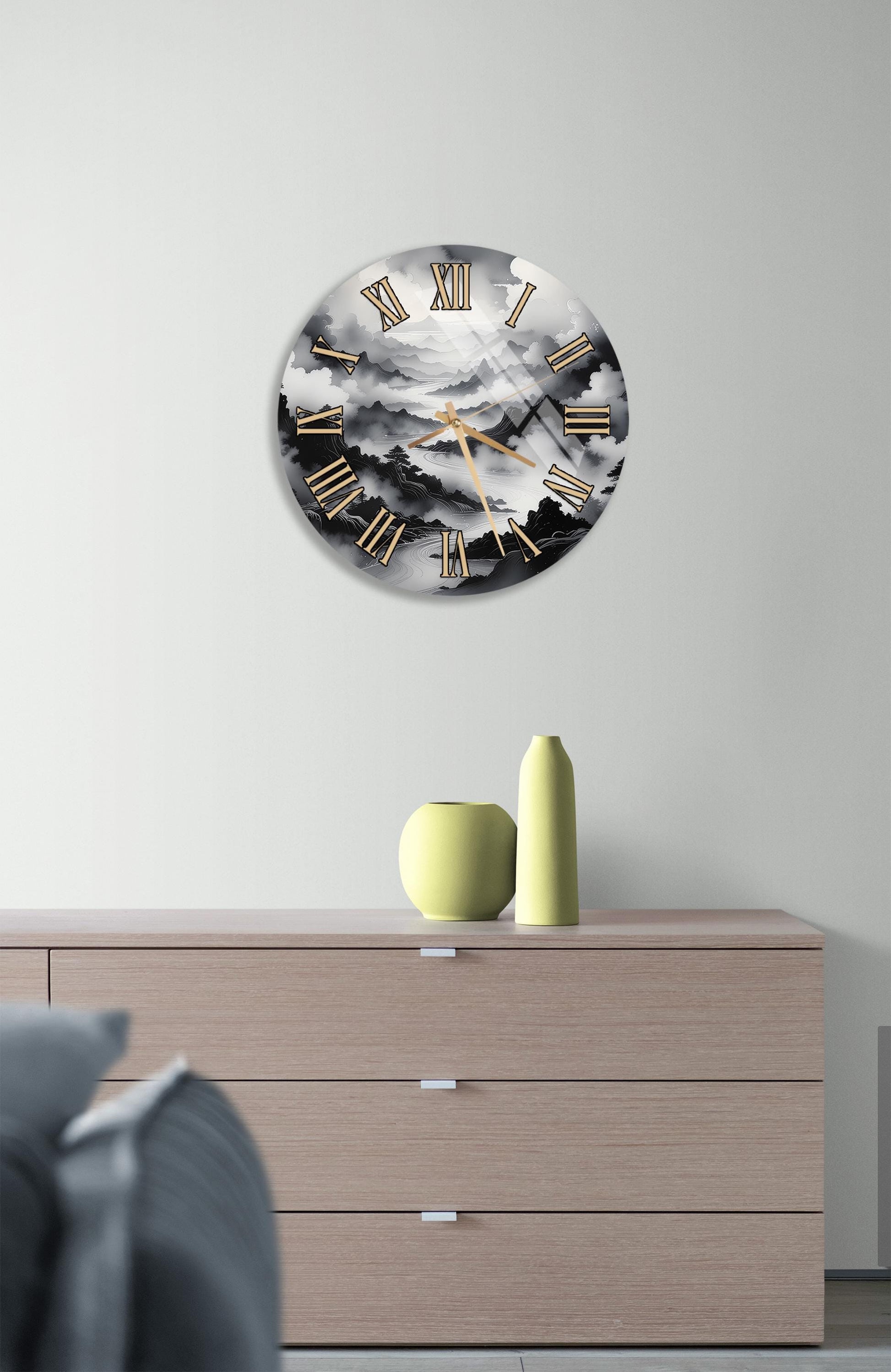 a wall clock with a black and white design, mounted on a wall above a wooden dresser with three drawers.
