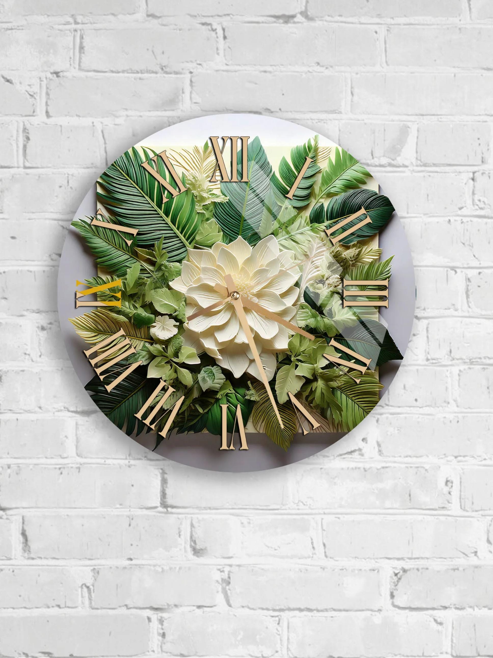 A round clock with a white face and gold Roman numerals, surrounded by a lush arrangement of green leaves and a large white flower.