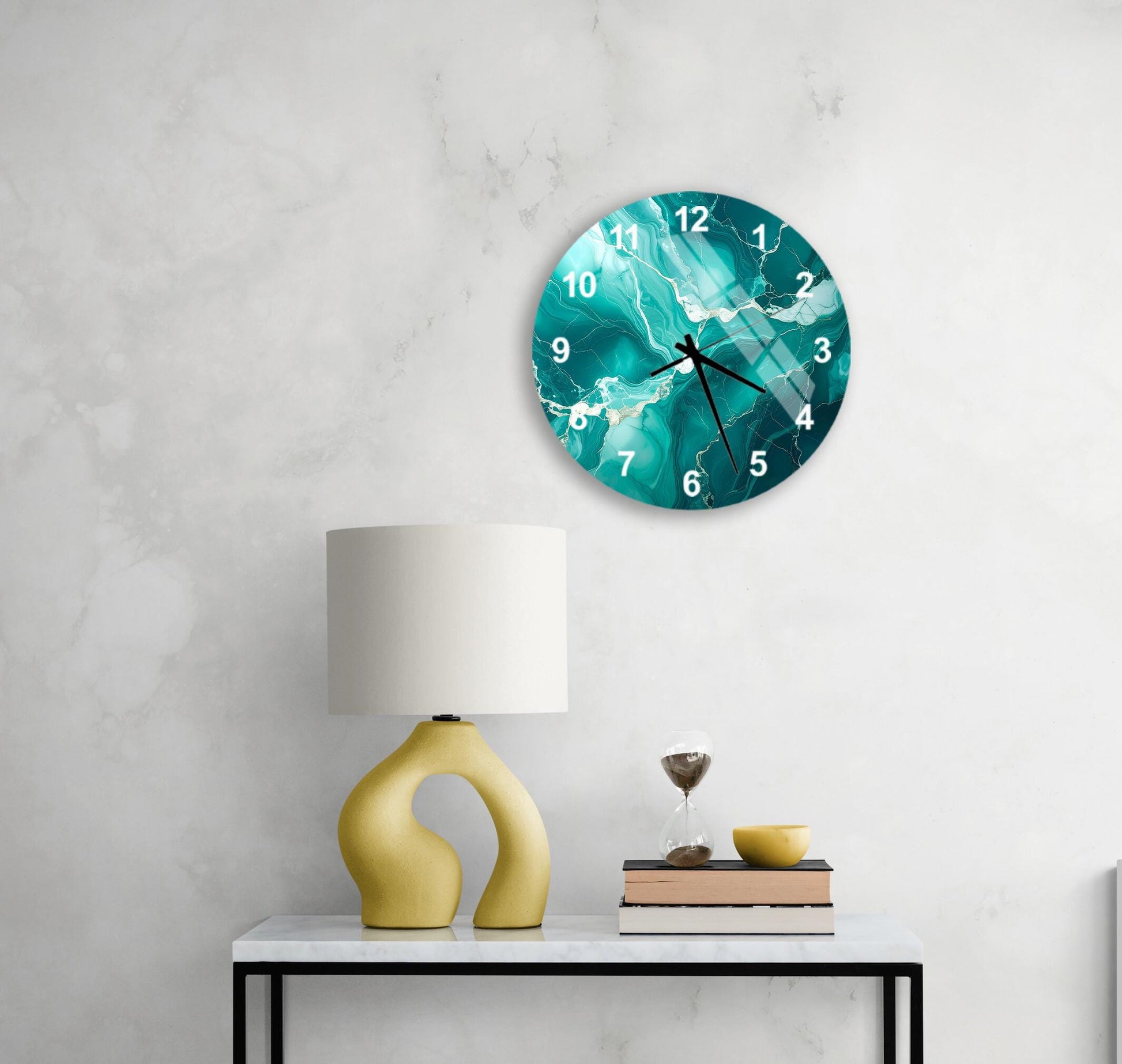 a modern wall clock with a turquoise and white design, mounted on a white wall above a white table with a yellow lamp and a stack of books.
