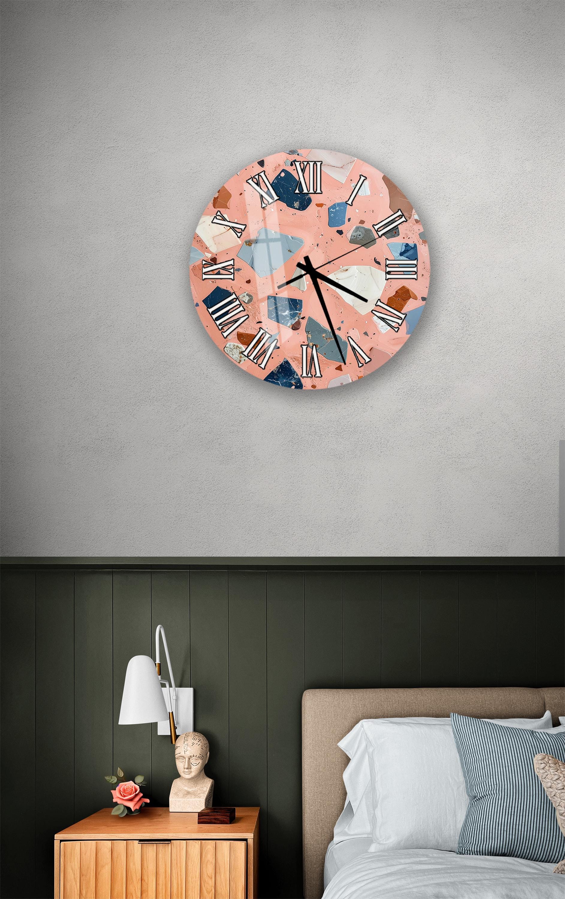 a bedroom setting with a large, colorful clock hanging on the wall above a bed. The clock has a unique, abstract design with a mix of pink, blue, and white colors. The room also includes a nightstand with a lamp and a small statue or bust.