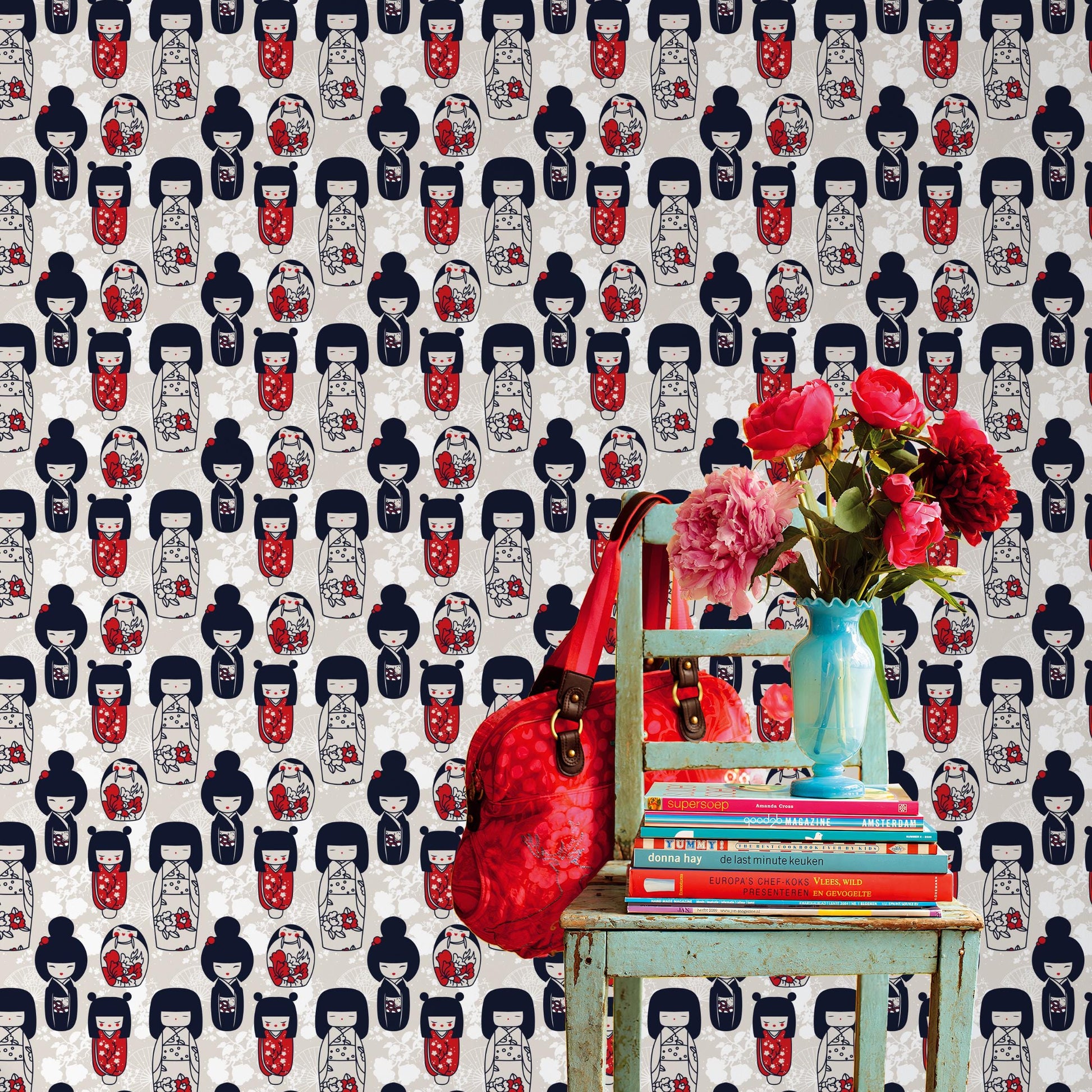 a vibrant scene with a green chair, a stack of books, a red handbag, and a vase of red flowers against a wall with a repeating pattern of Japanese-style dolls.