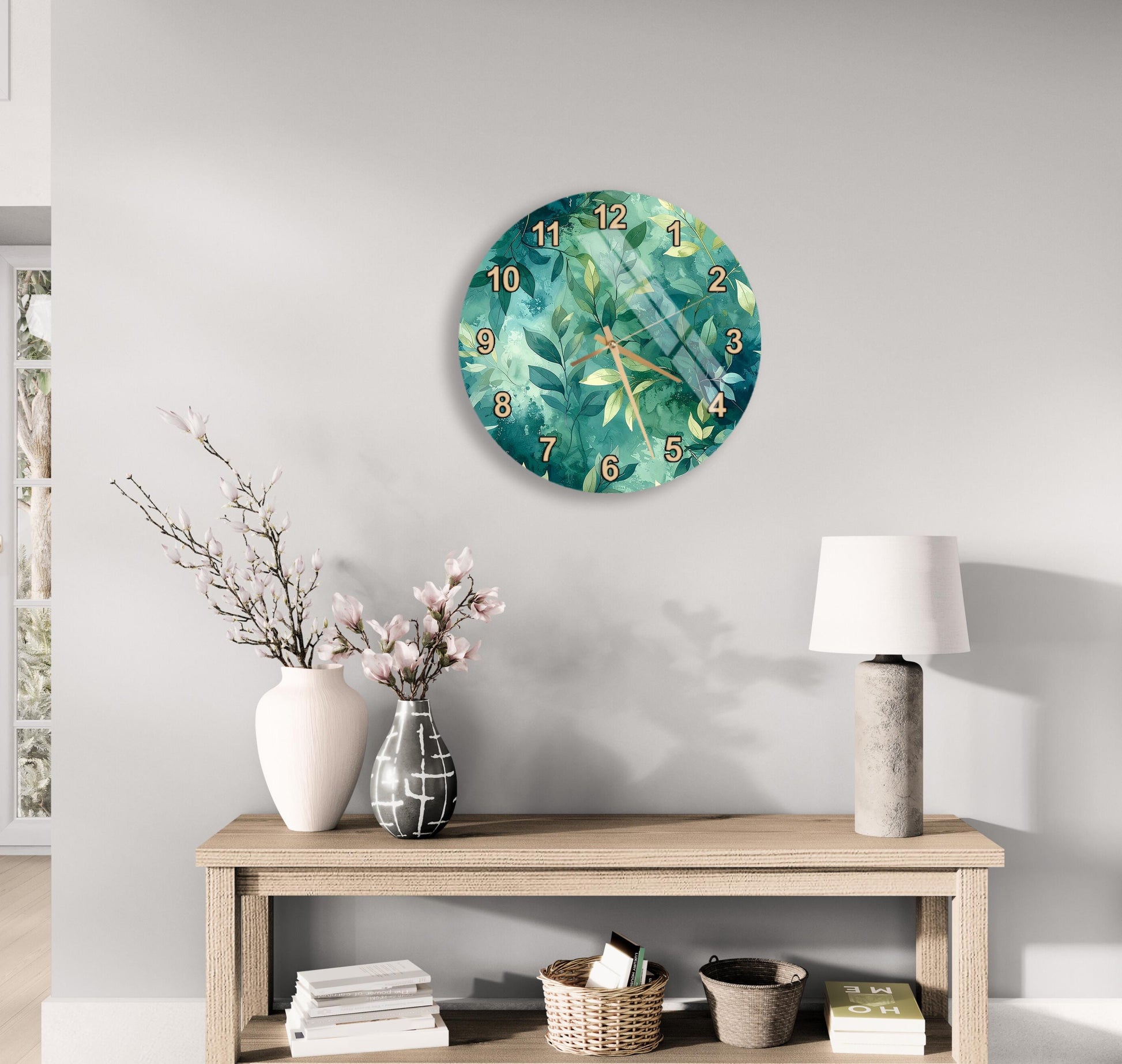 a wall clock with a green leaf design, a wooden table with a lamp, a vase with pink flowers, and a stack of books.