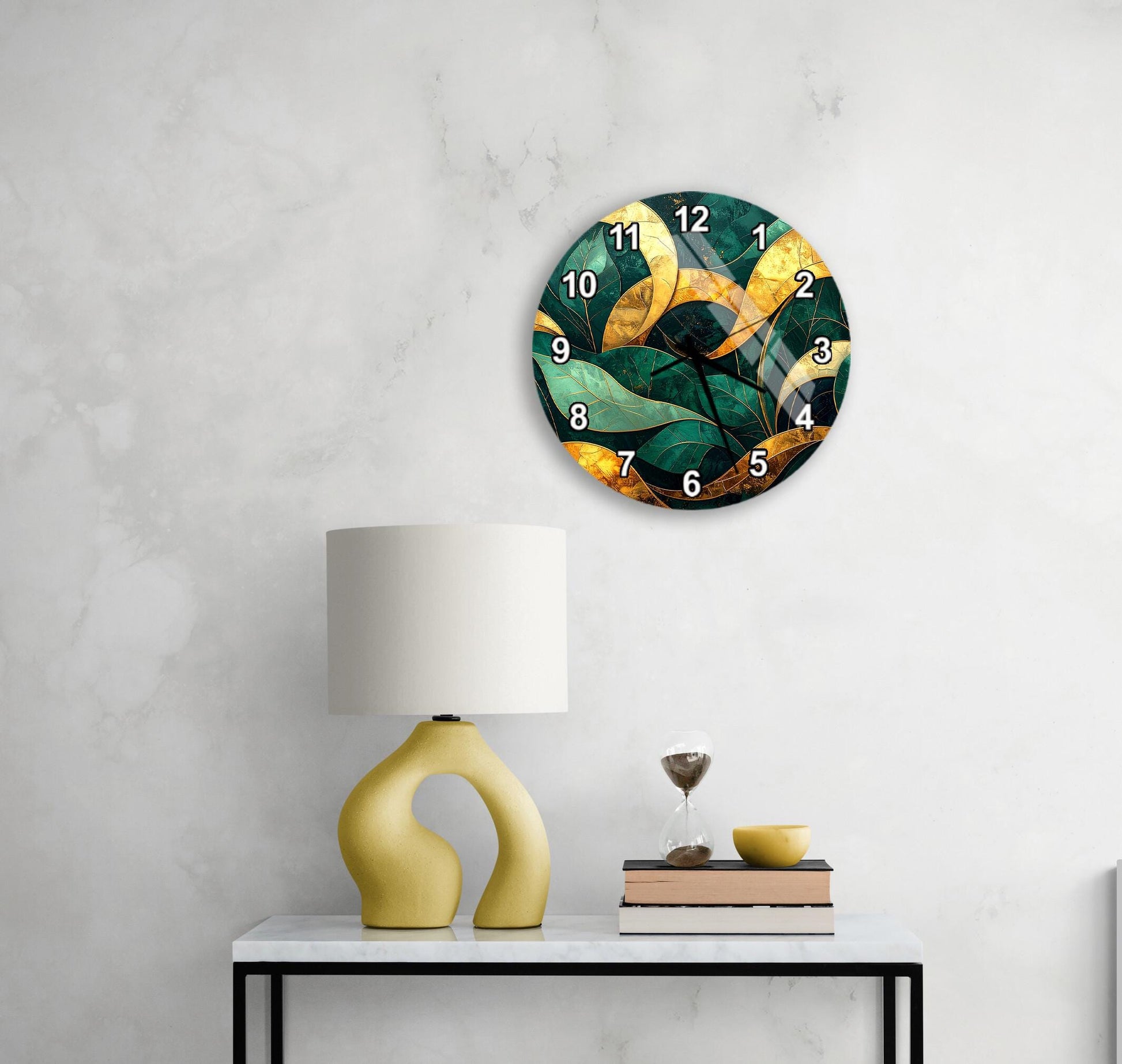 a modern clock with a green and gold design, mounted on a wall above a white table with a yellow lamp and a stack of books.