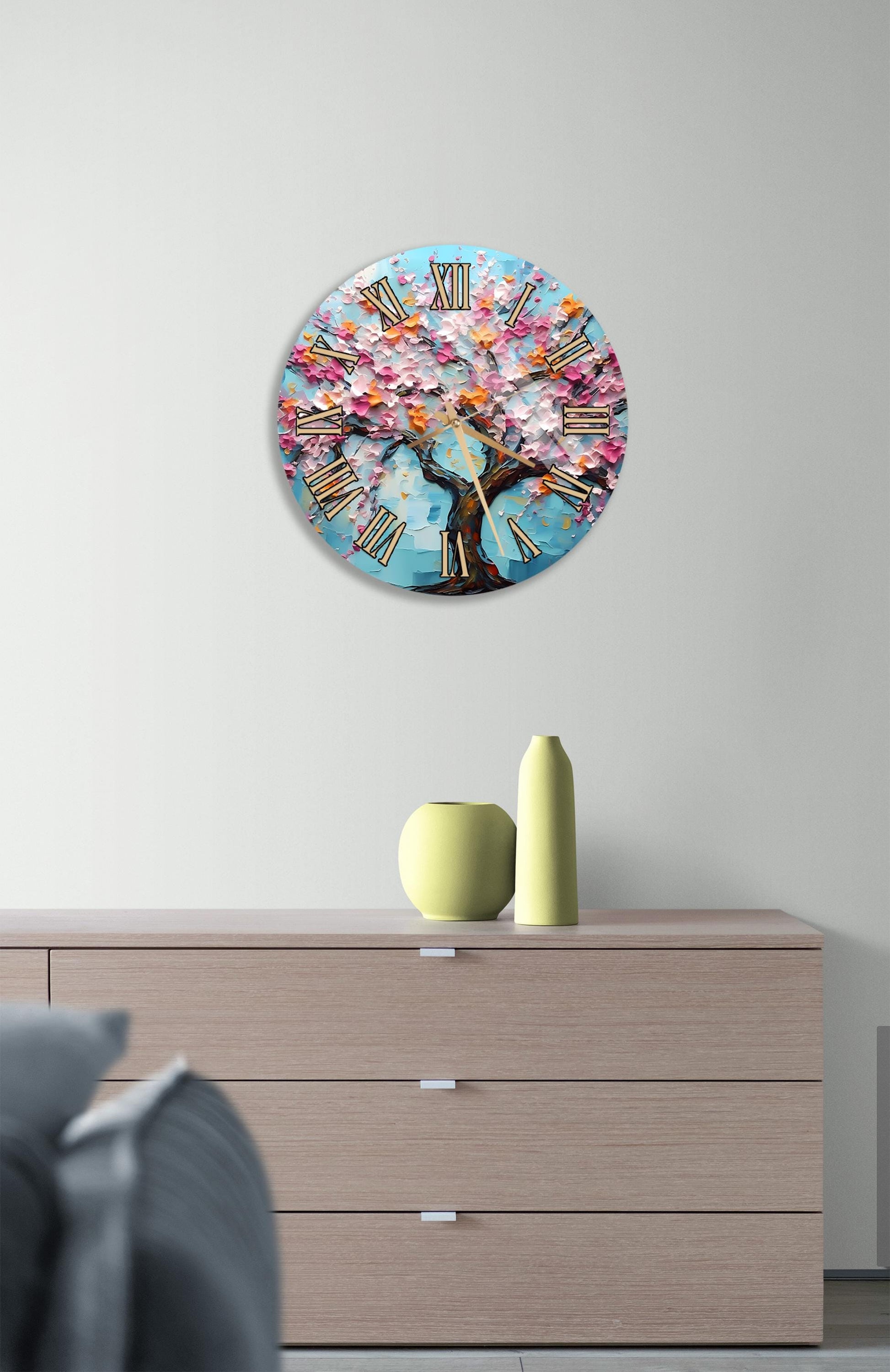 a round clock with a tree design on it, mounted on a wall above a wooden dresser.