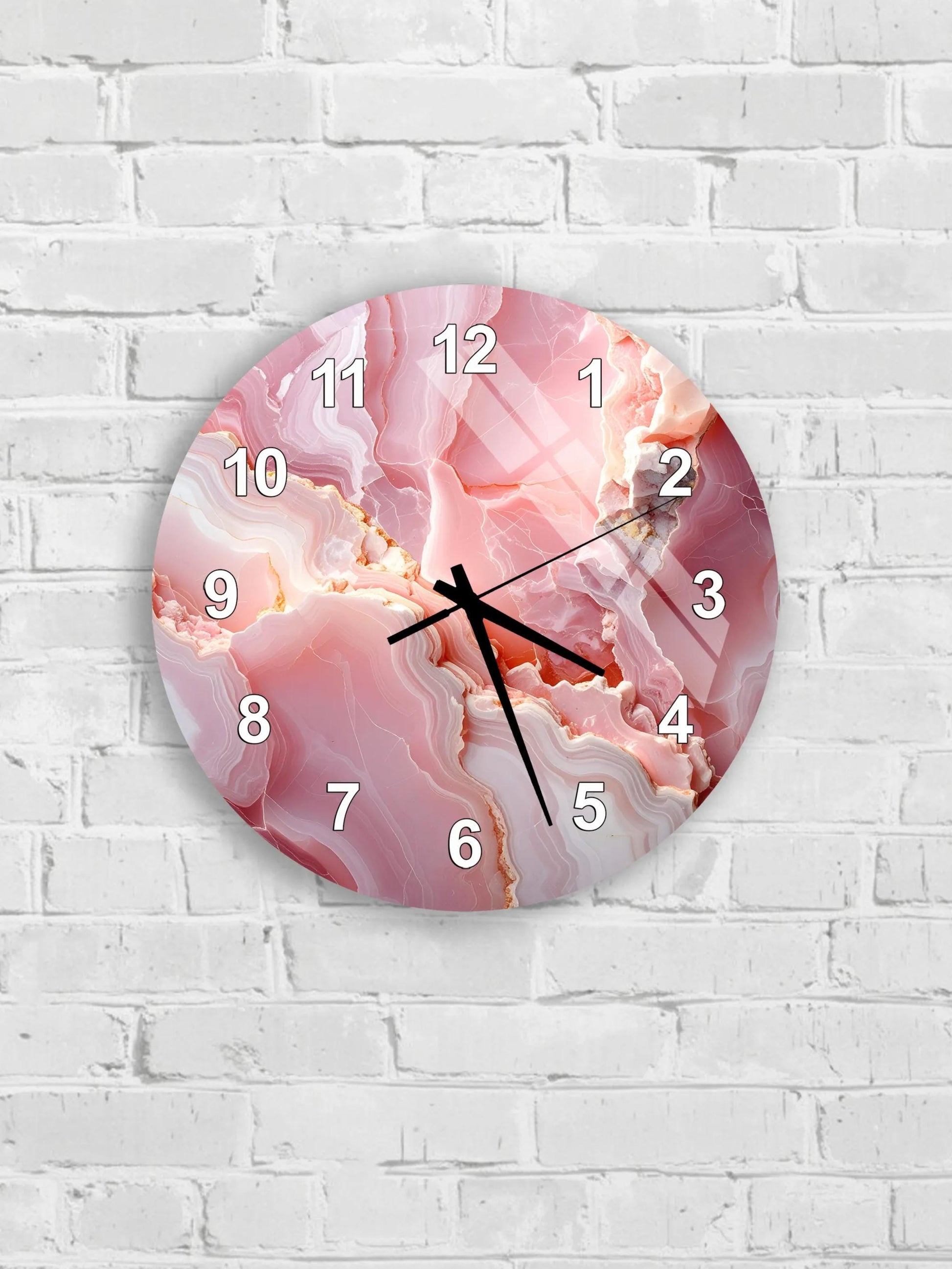 A round wall clock with a pink marble-like design on its face, mounted on a white brick wall.