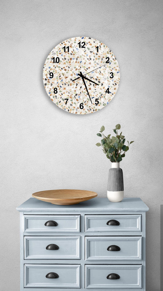 a wall clock with a speckled pattern, a wooden bowl, and a vase with greenery on a light blue dresser.