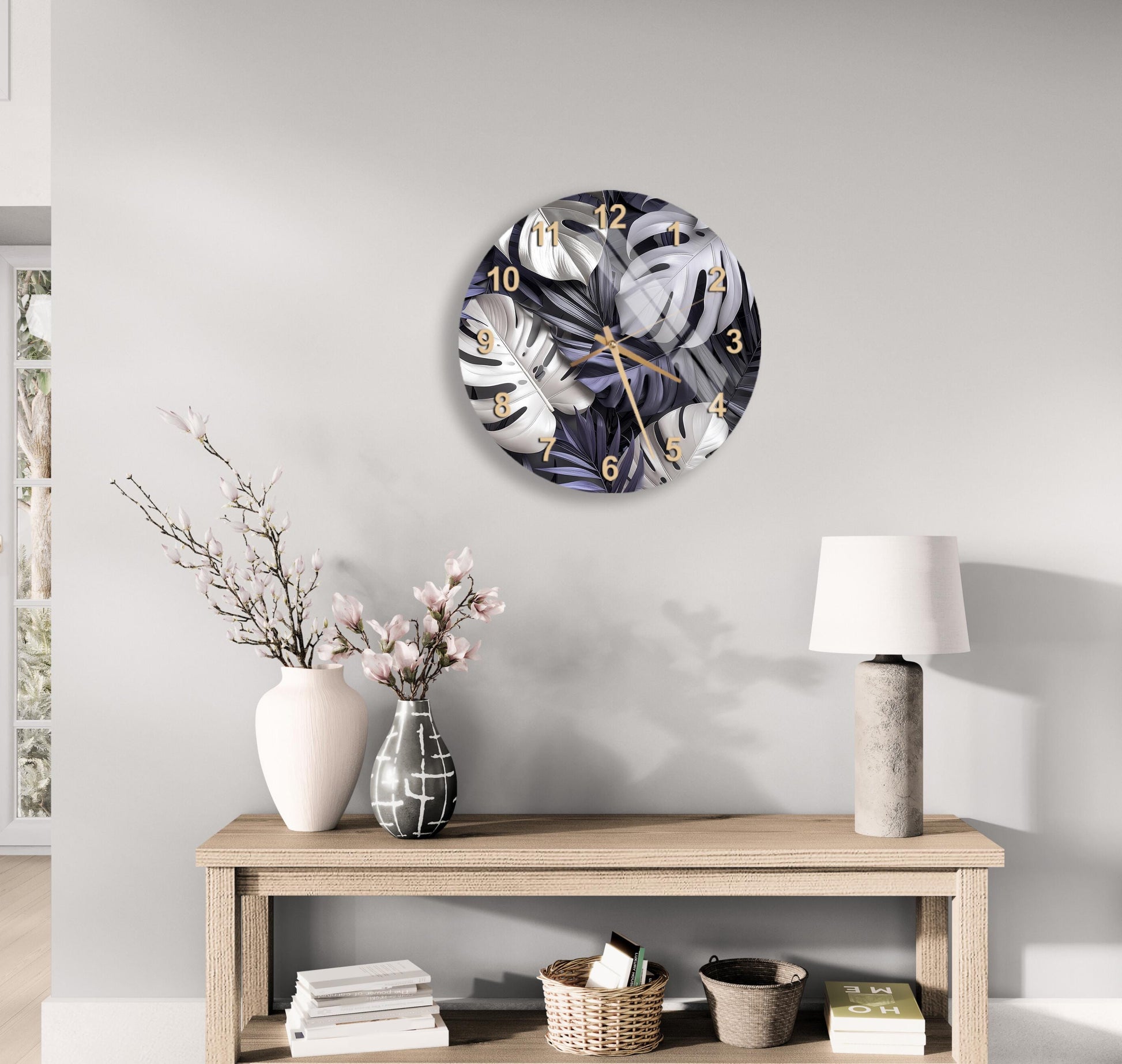 a modern living room with a round wall clock displaying a leafy plant design, a wooden table with a lamp, a vase with pink flowers, and a stack of books.
