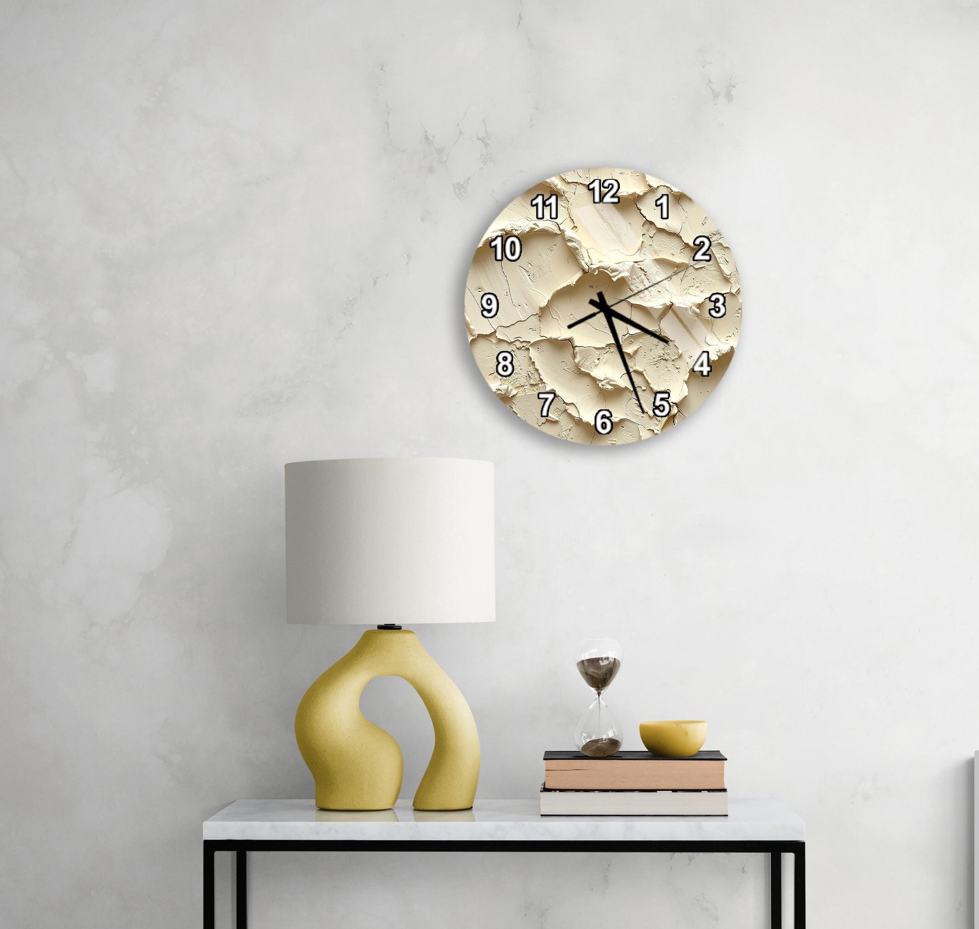 a modern, minimalist living space with a white wall, a round clock with a unique design, a yellow lamp, a stack of books, and a glass of wine on a white table.