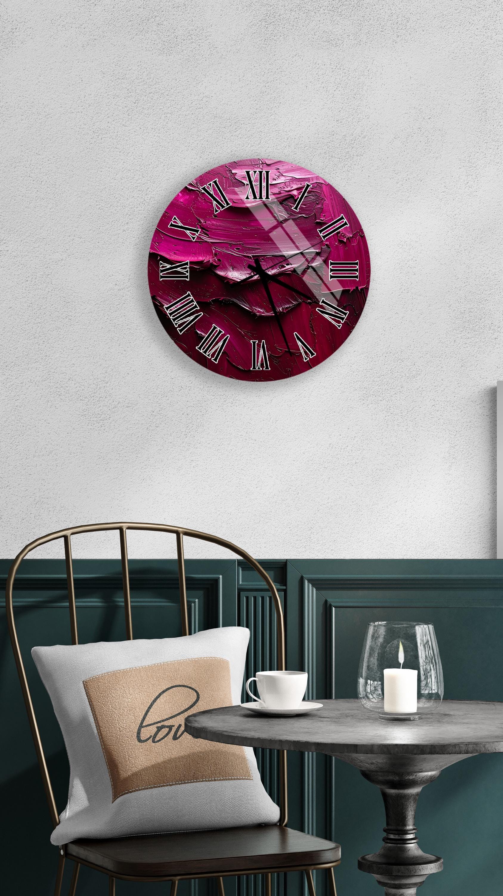 a round wall clock with a pink and purple color scheme, mounted on a white wall above a dining table with a white tablecloth. The table is set with a white cup and a candle, creating a cozy and inviting atmosphere.