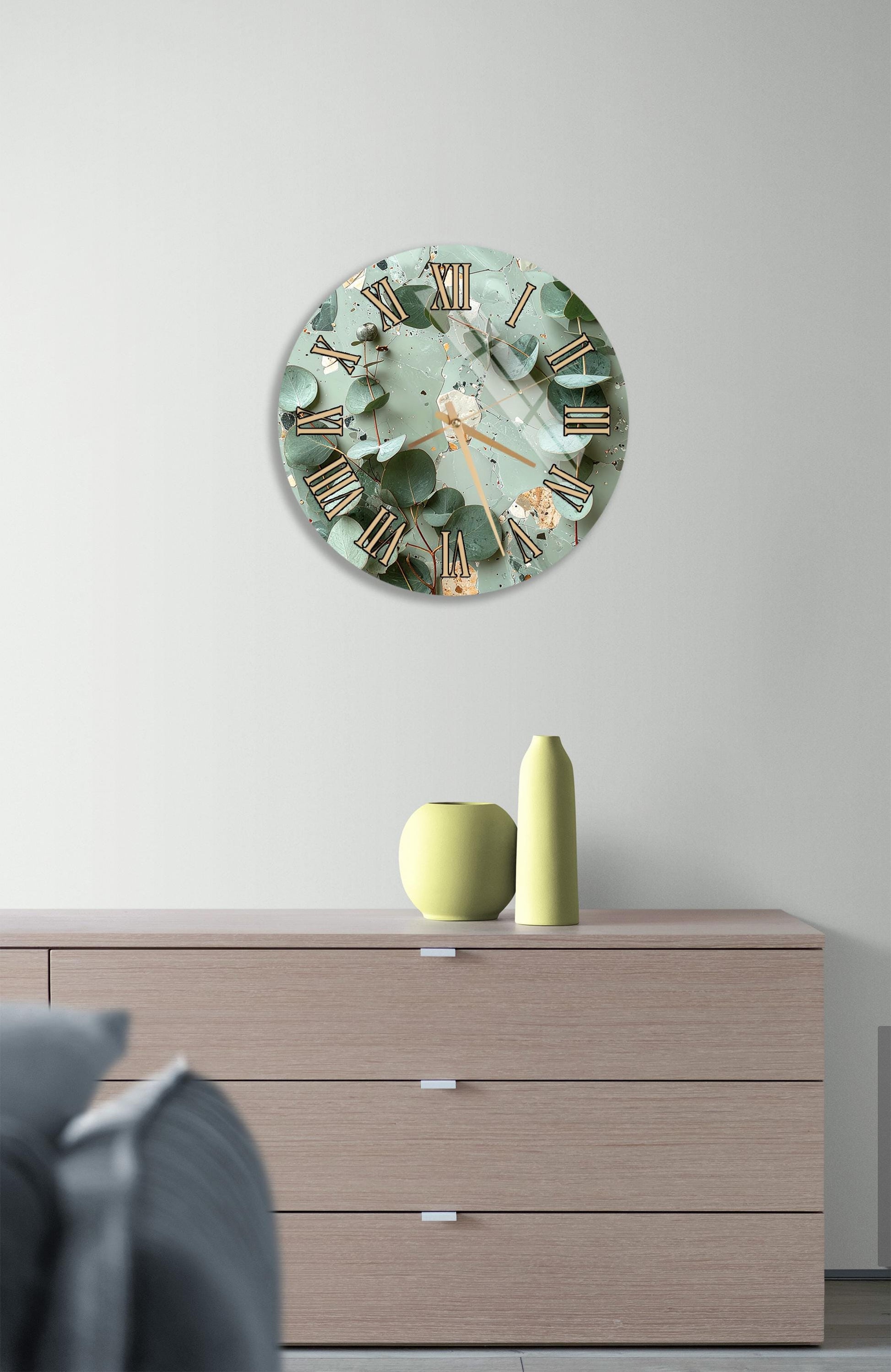 a wall clock with a green and gold design, mounted on a wall above a wooden dresser with three drawers.