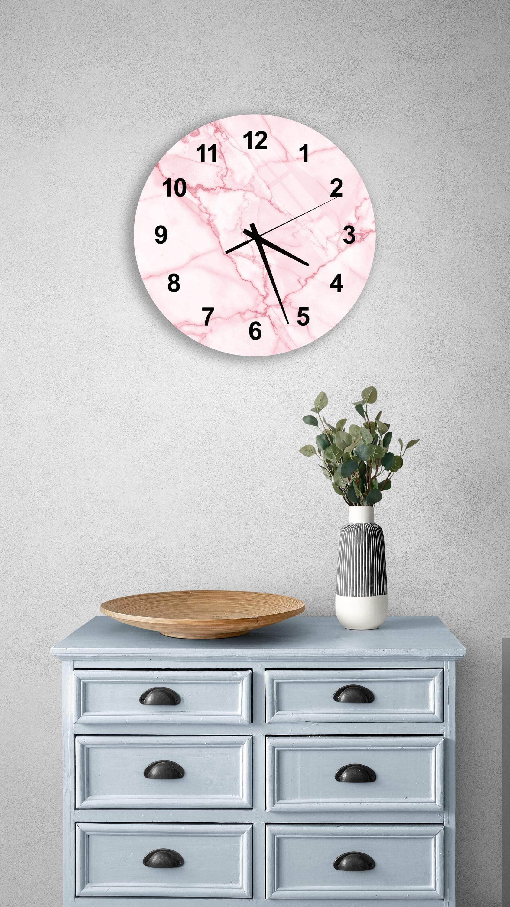 a wall clock with a pink marble design, mounted on a wall above a light blue dresser with six drawers. The dresser also has a wooden tray and a vase with greenery on it.