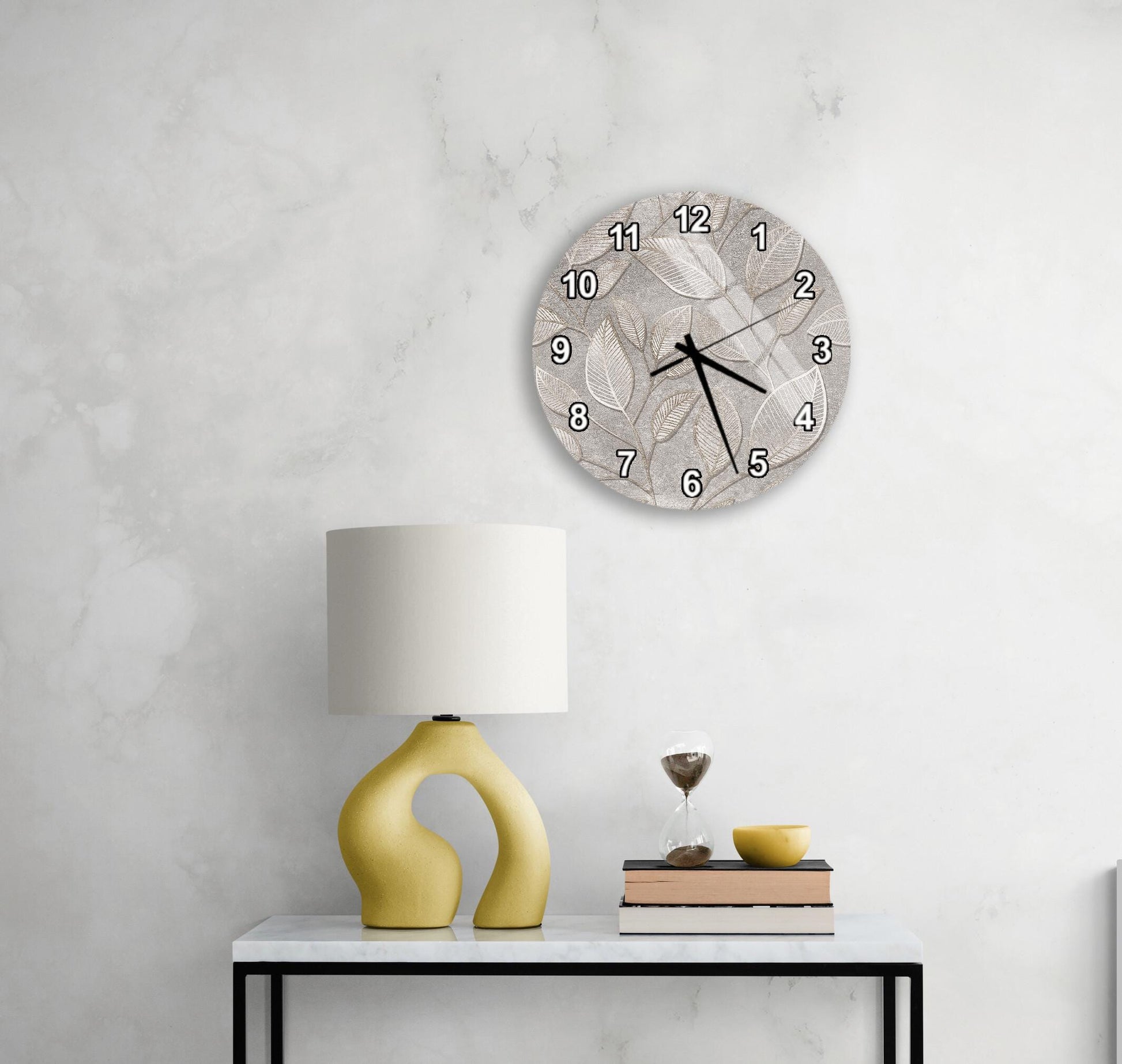 a modern living room with a white marble wall, a round clock with a leaf design, a yellow lamp with a unique curved base, and a small table with a book and a glass of wine.