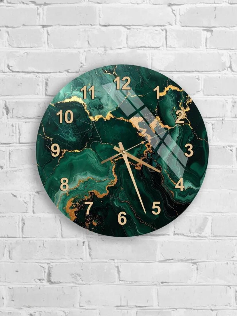 A wall clock with a green marble-like design and gold numbers is mounted on a white brick wall.