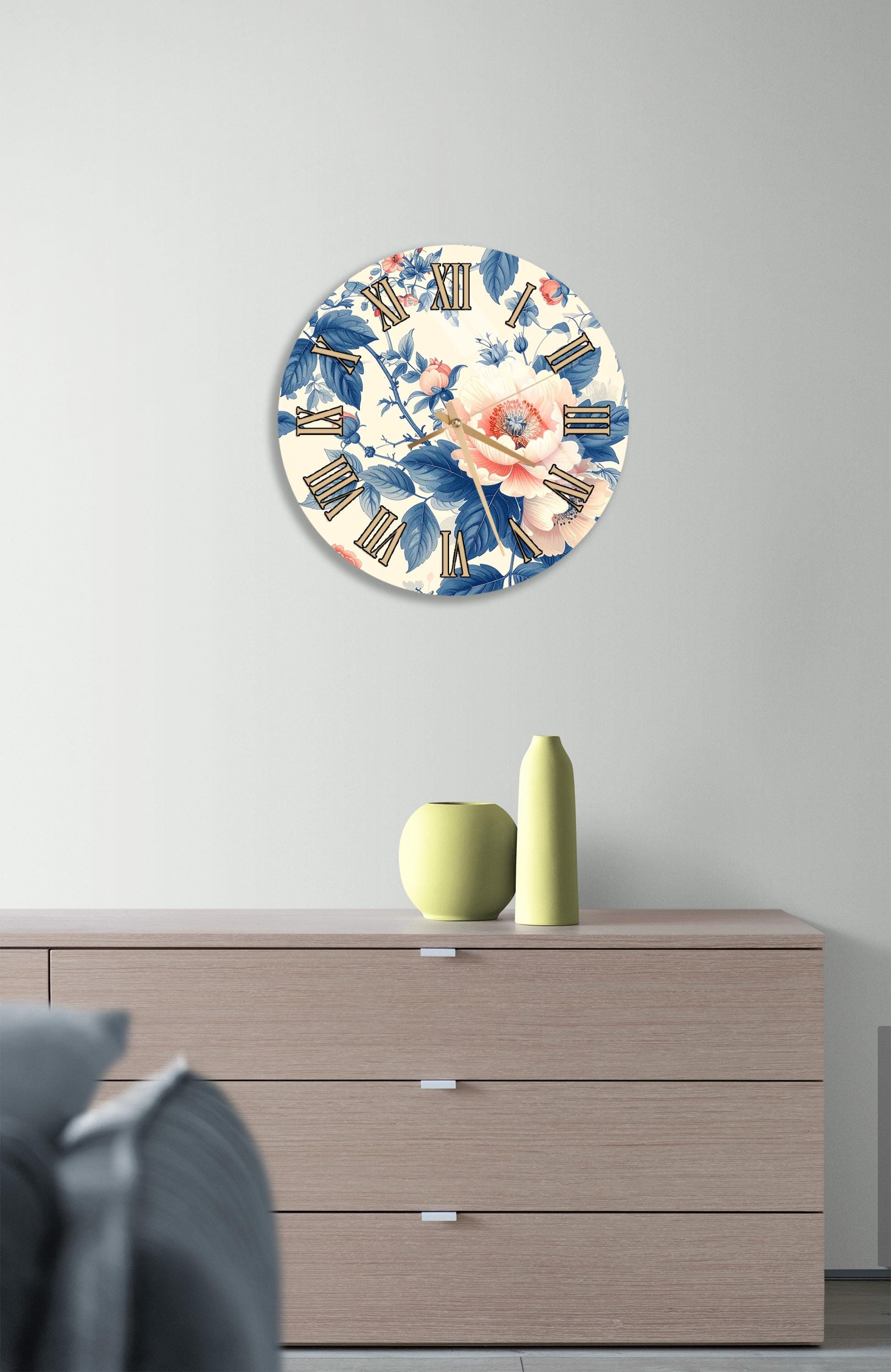 a wall clock with a floral design, mounted on a wall above a wooden dresser with three drawers.