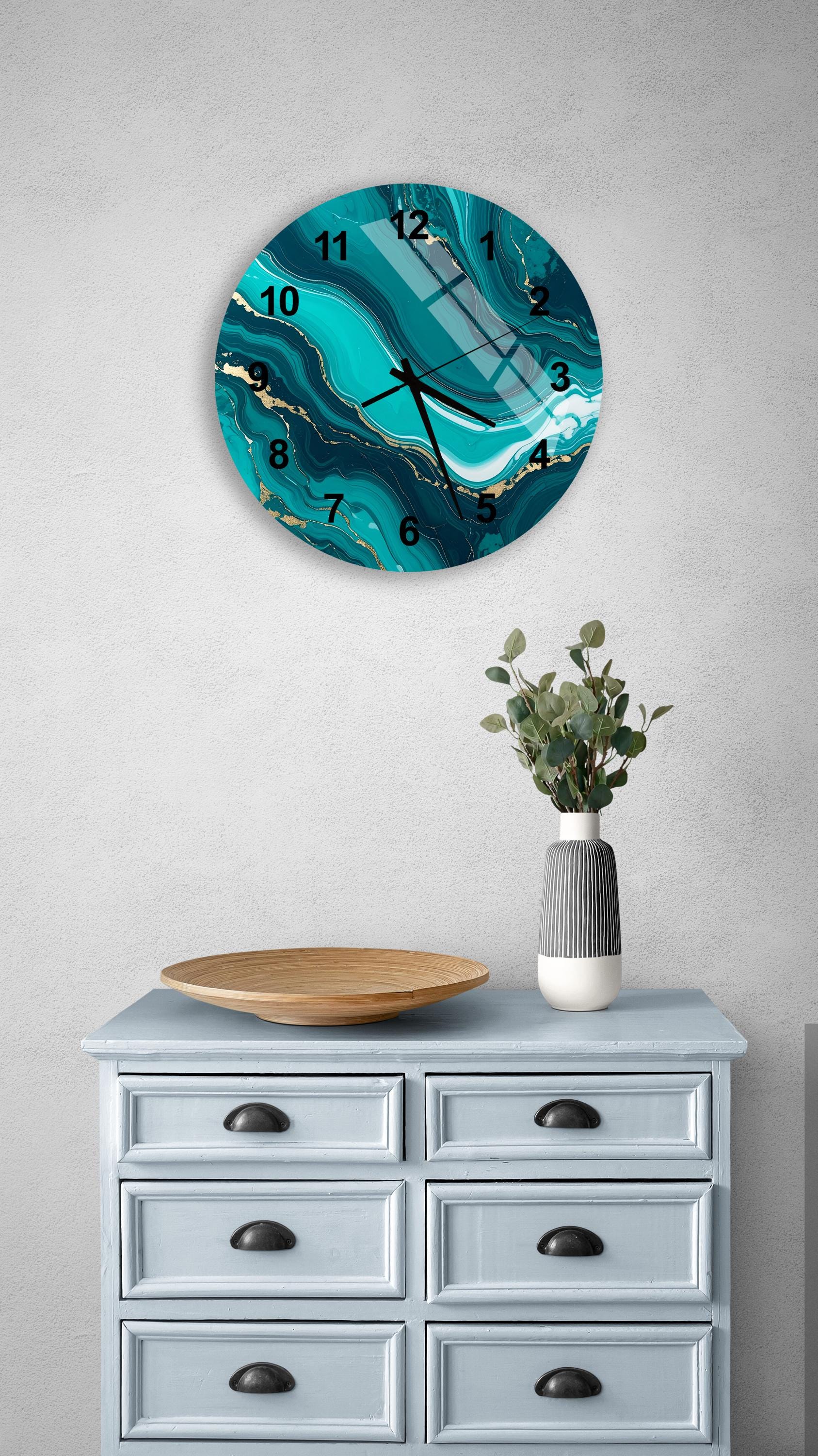 a wall clock with a turquoise marble design, mounted on a wall above a light blue dresser with six drawers. The dresser also has a vase with greenery and a wooden tray on top.