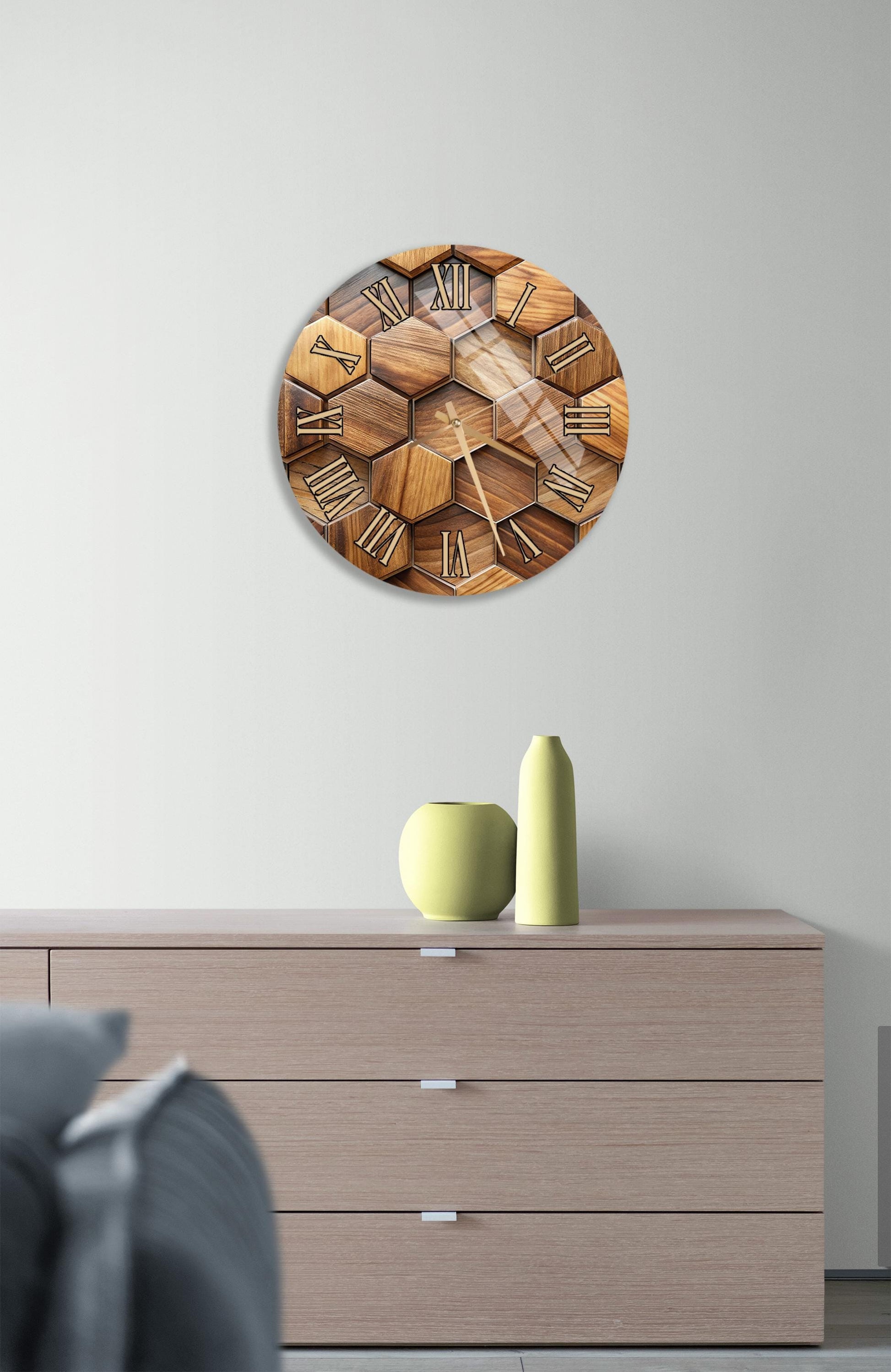 a wooden clock with a hexagonal design, mounted on a wall above a wooden dresser with three drawers. The dresser also has a small green vase and a yellow vase on it.