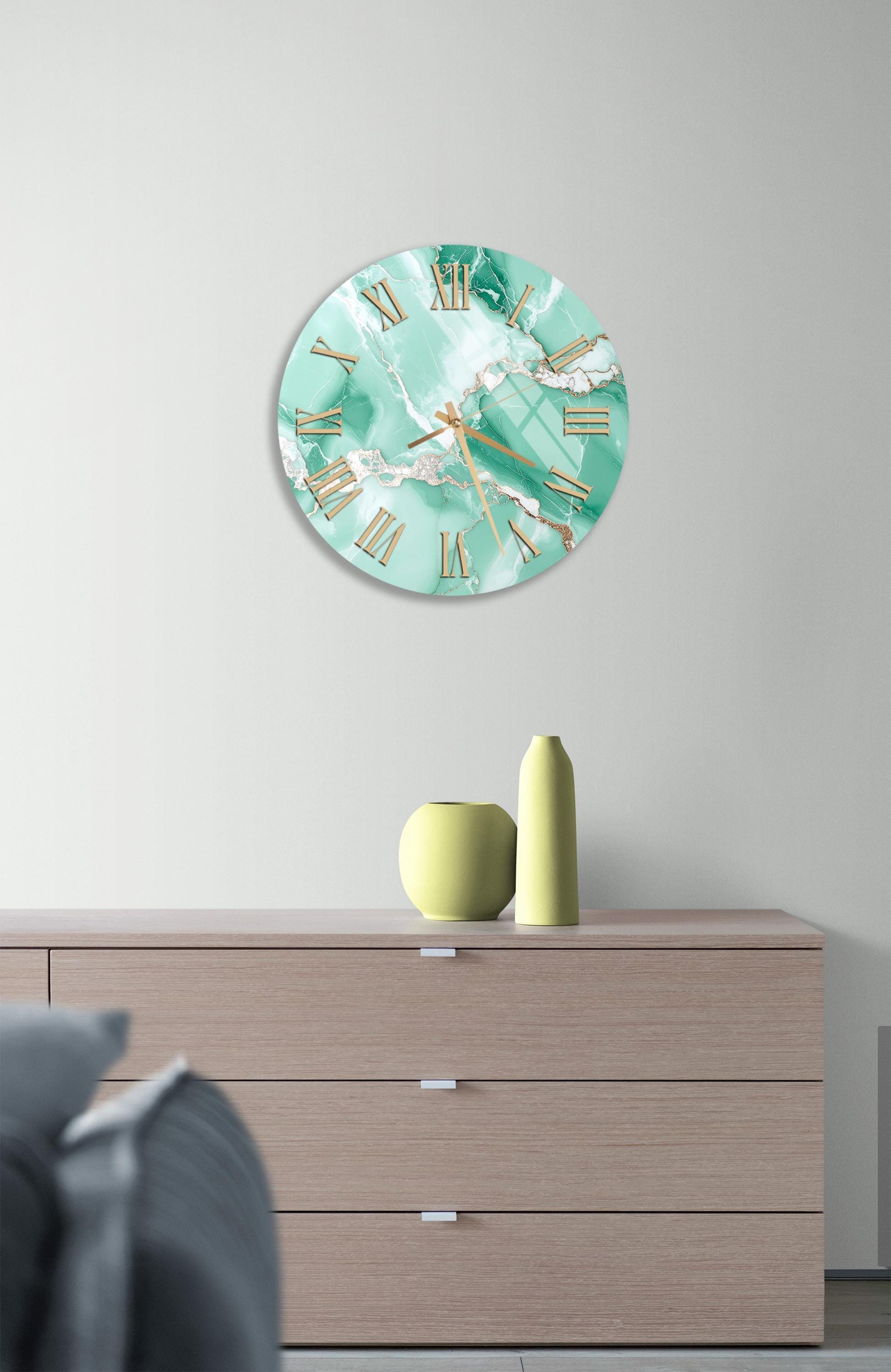 a wall clock with a marble-like design, mounted on a wall above a wooden dresser with three drawers. The dresser also has a small vase and a yellow bottle on it.