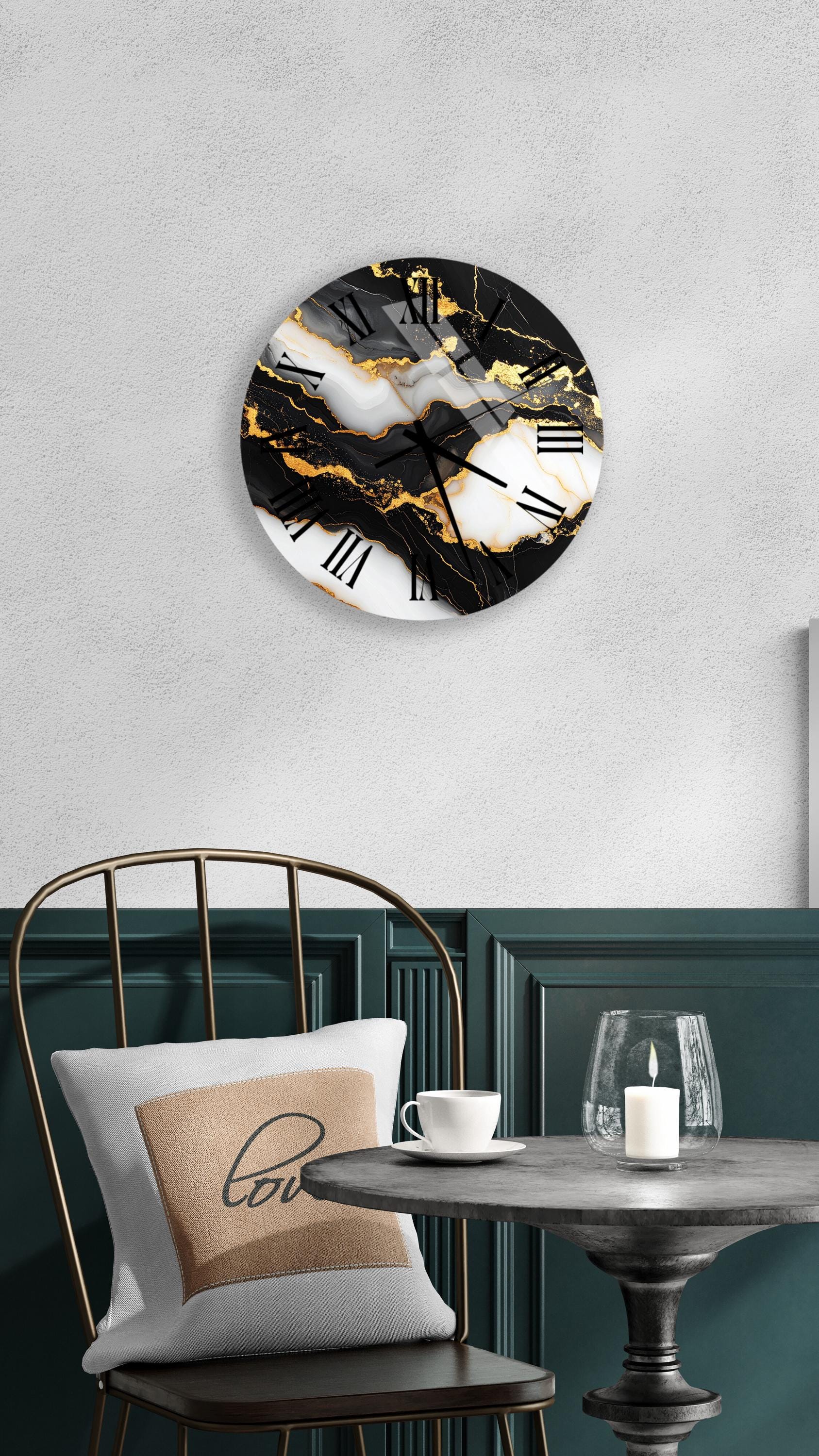 a modern black and white clock with a marble-like design, mounted on a wall above a table with a white tablecloth. The table has a glass candle holder and a white coffee cup on it. A white pillow with the word "love" printed on it is also present on the table.