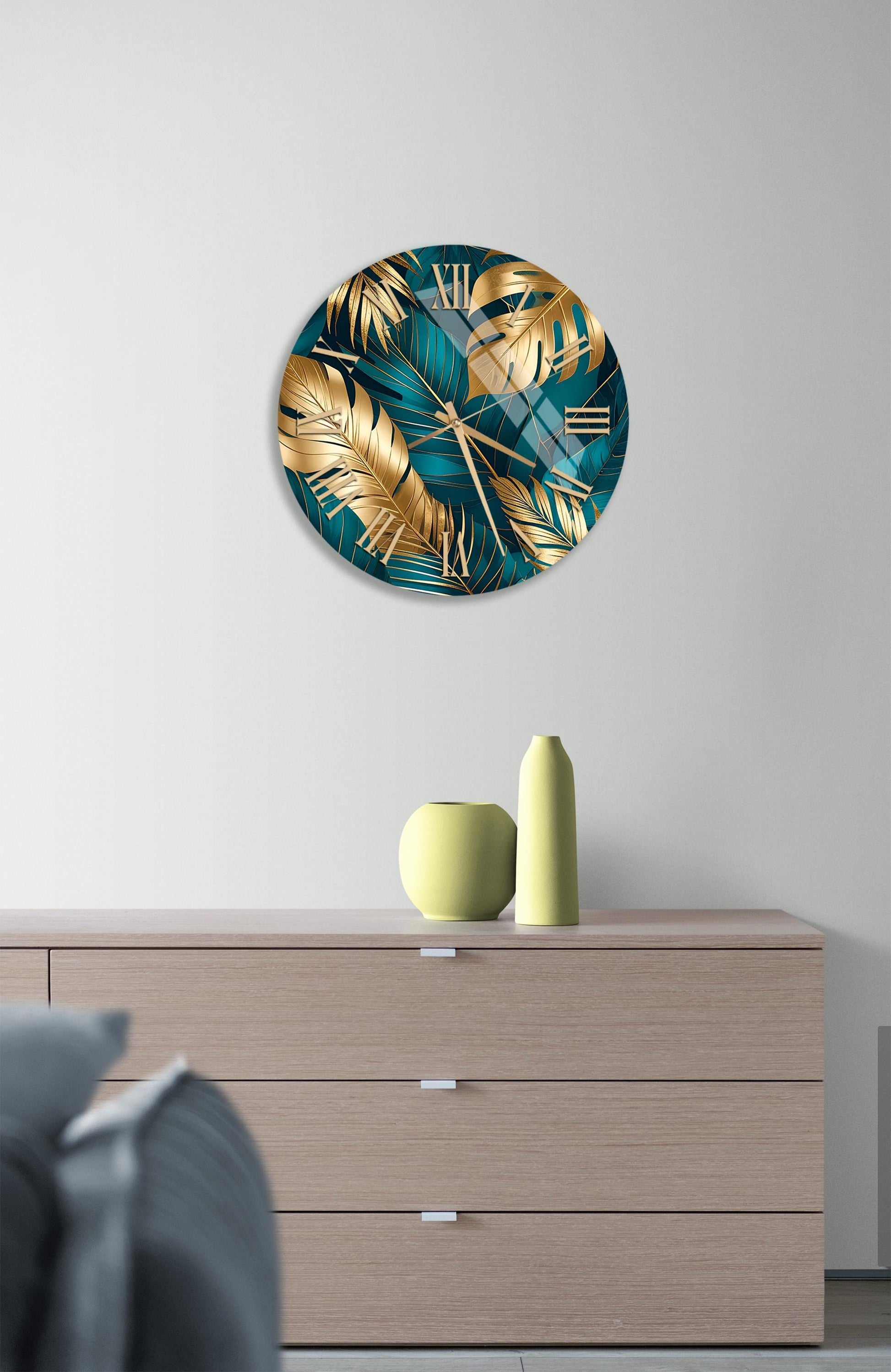 a modern living room with a large round clock featuring a tropical leaf design on the wall above a wooden dresser. The dresser has a vase and a small sculpture on top of it.