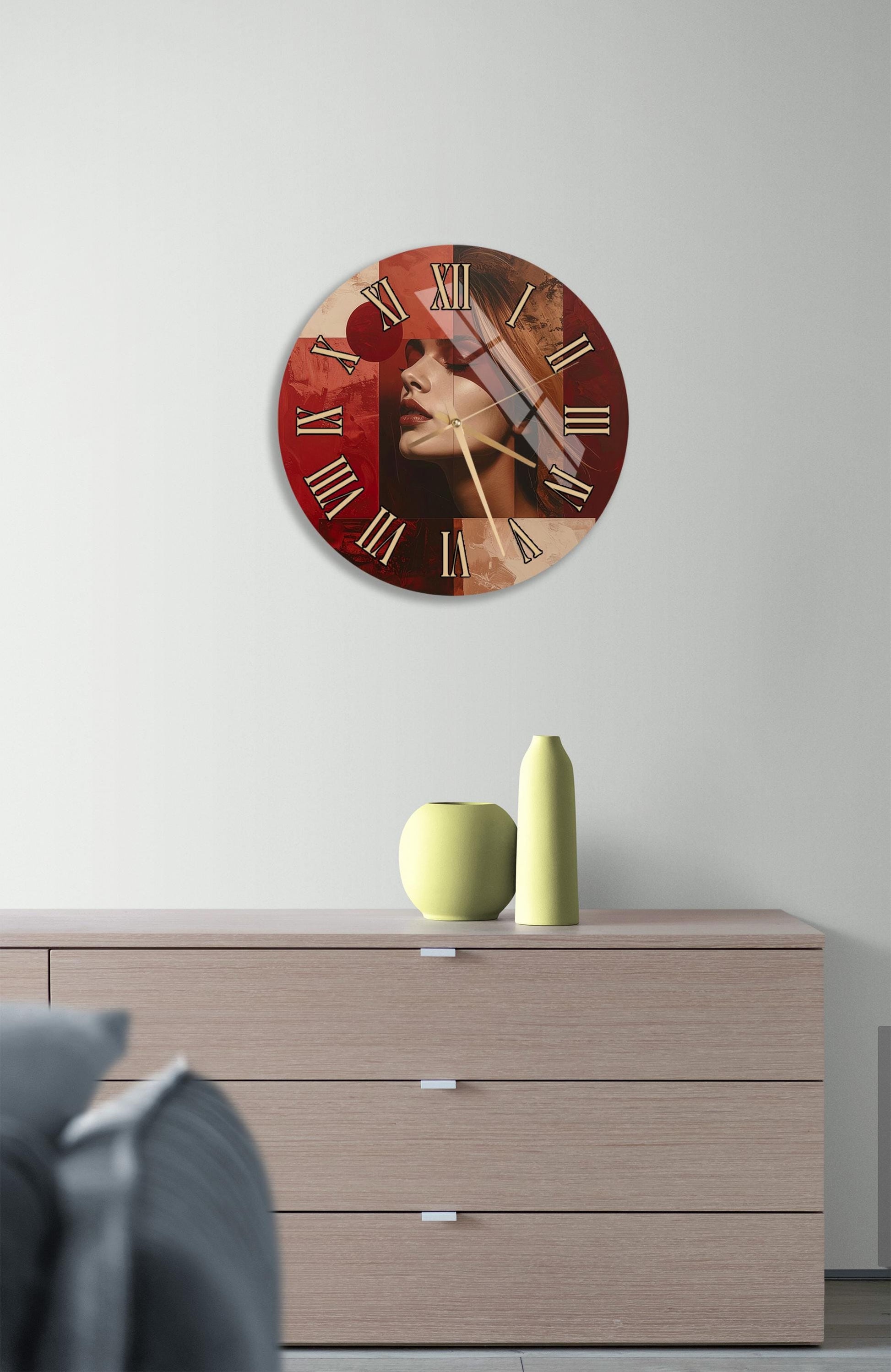 a wall clock with a red and brown color scheme, mounted on a wall above a wooden dresser. The dresser has three drawers and contains a yellow vase and a small green pot.