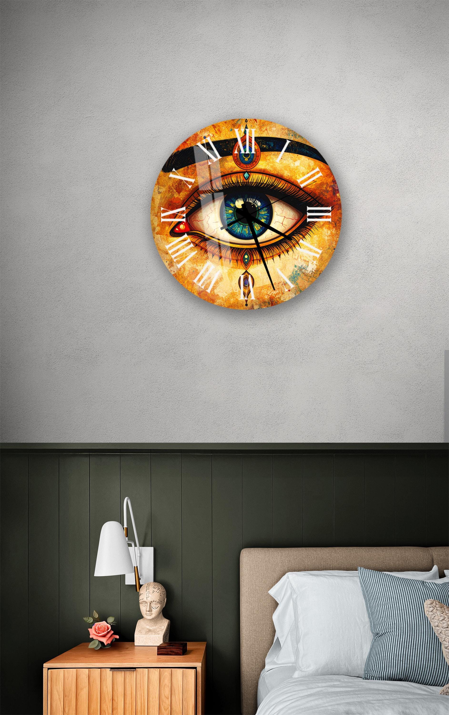 a wall clock with an eye design on it, mounted on a wall above a bedside table with a lamp and a small statue.