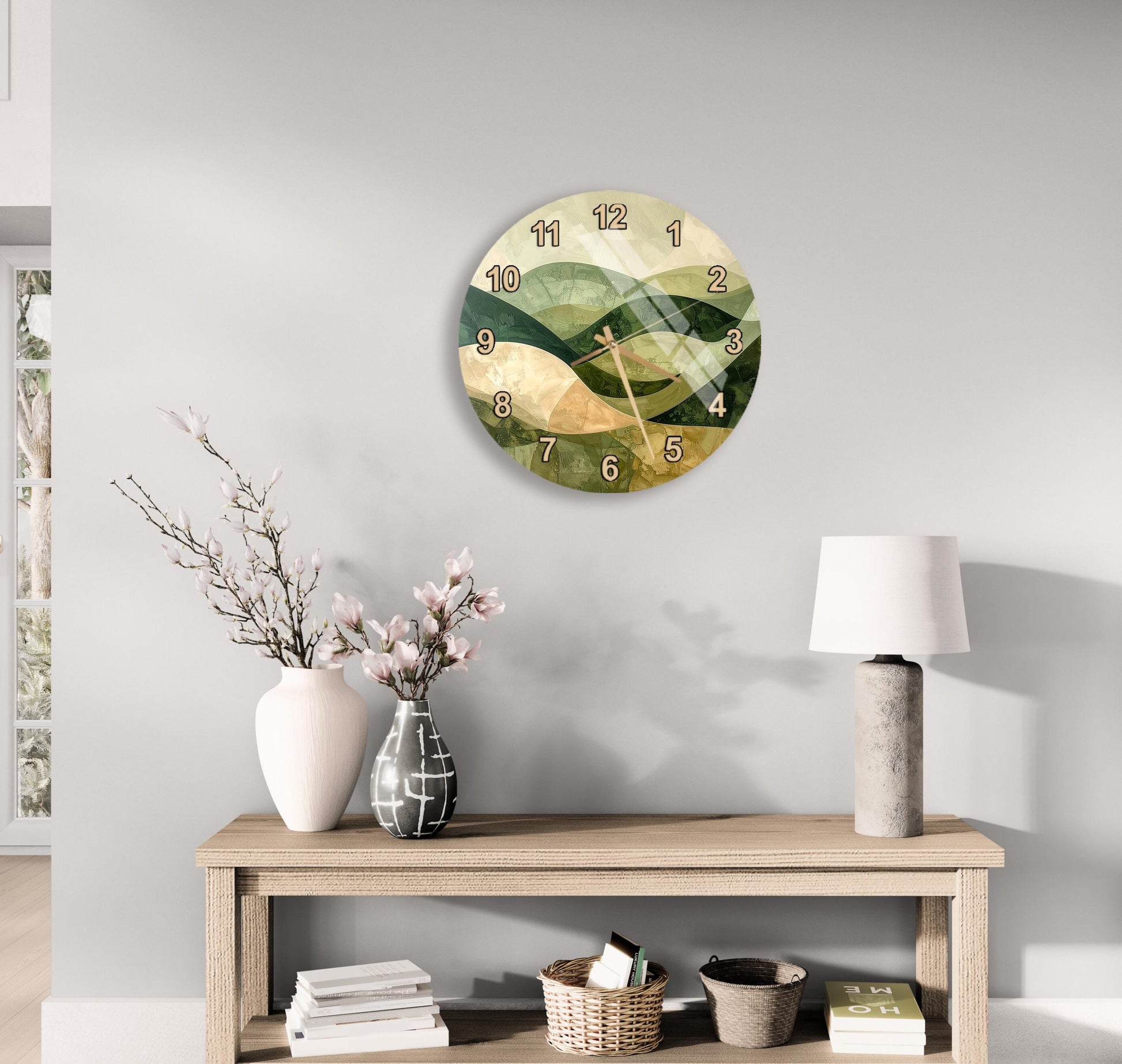a wall clock with a landscape design, a wooden table with a lamp, a vase with flowers, and some books on a shelf.