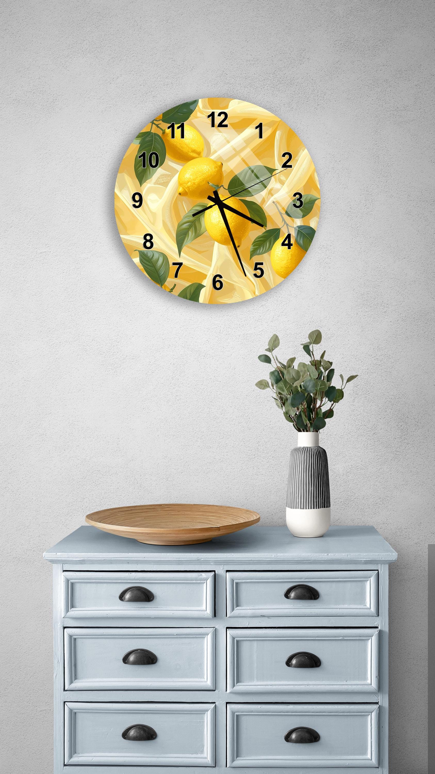 a wall clock with a yellow and green design, hanging above a light blue dresser with six drawers. The dresser also has a vase with greenery and a wooden tray on top.