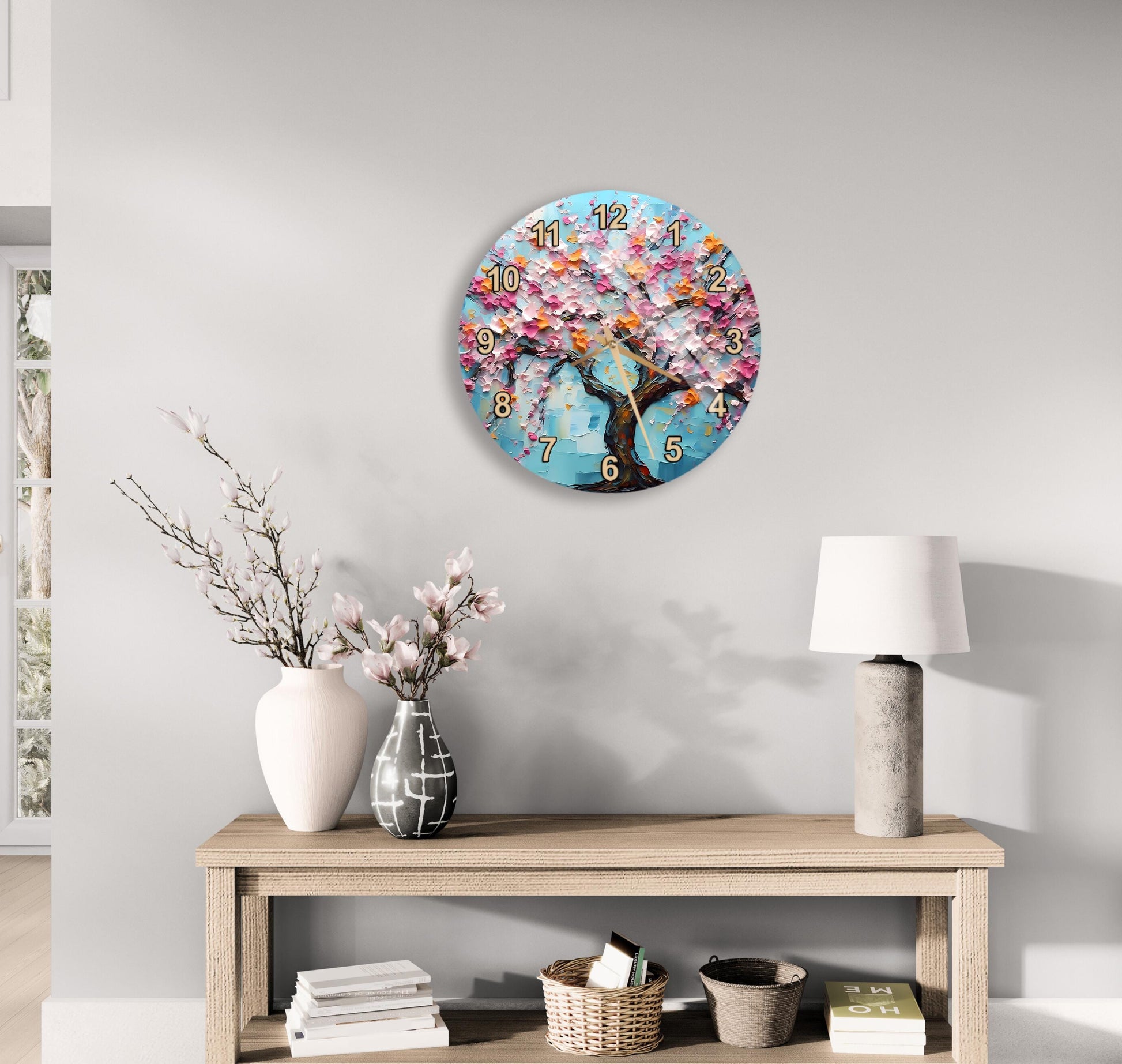 a wall clock with a floral design, a wooden table with a lamp, a vase with pink flowers, and a stack of books on a shelf.
