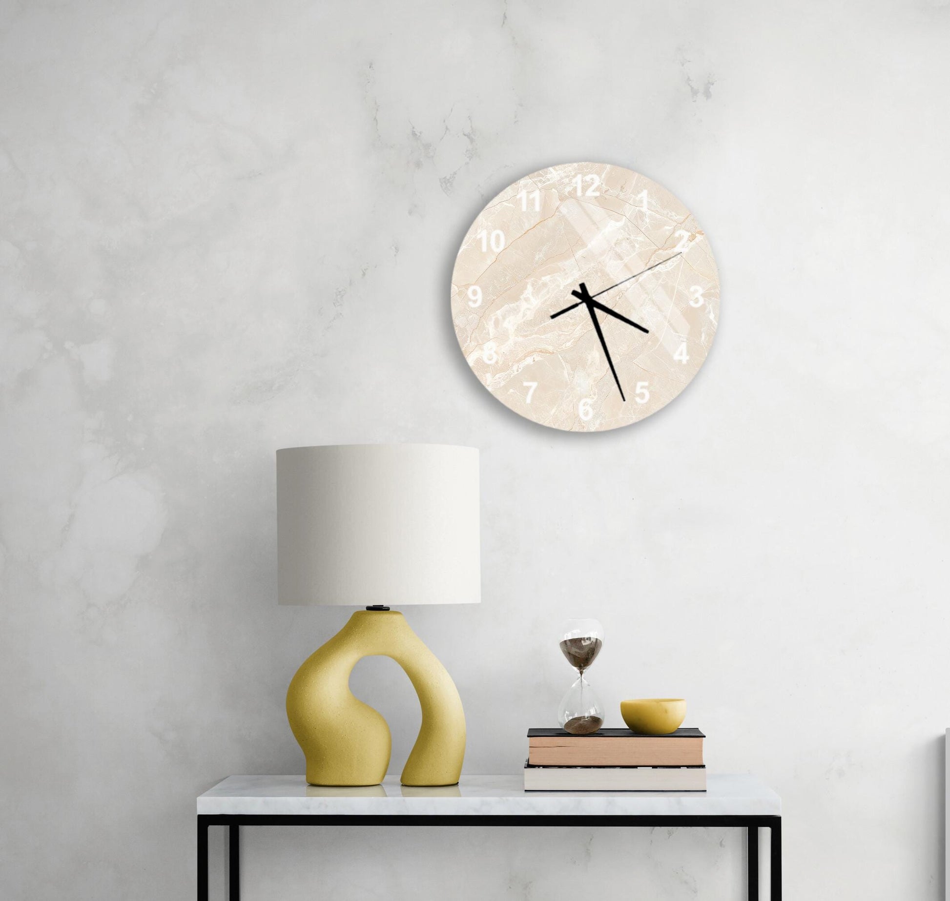 a modern living room with a white marble wall, a round clock with a beige and white design, a yellow lamp with a unique curved base, a stack of books, and a glass of wine on a white table.